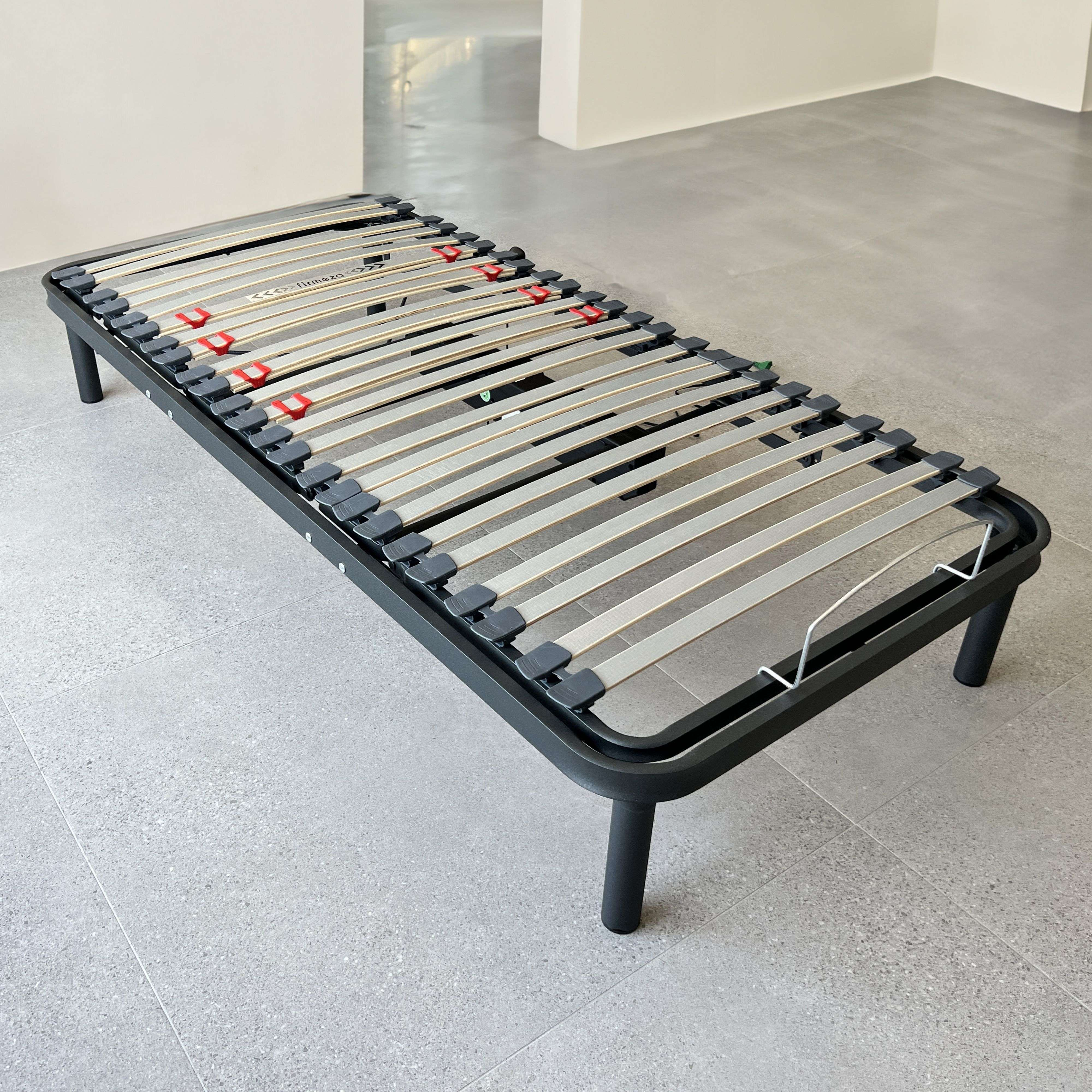 Una base de cama negra con lamas de madera sobre suelo de baldosas grises.