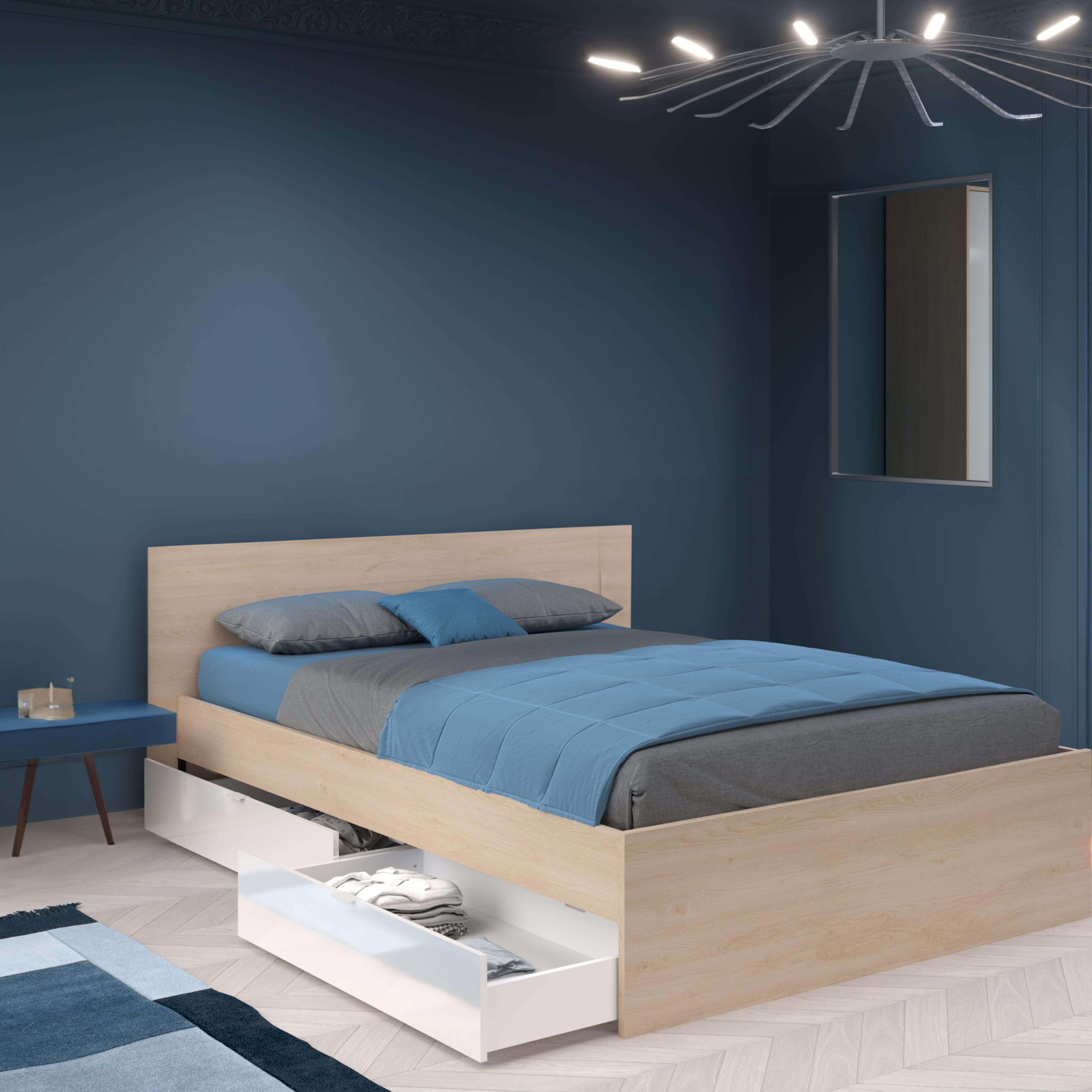 Una cama con ropa de cama azul y cajones debajo, en una habitación azul con luz moderna.