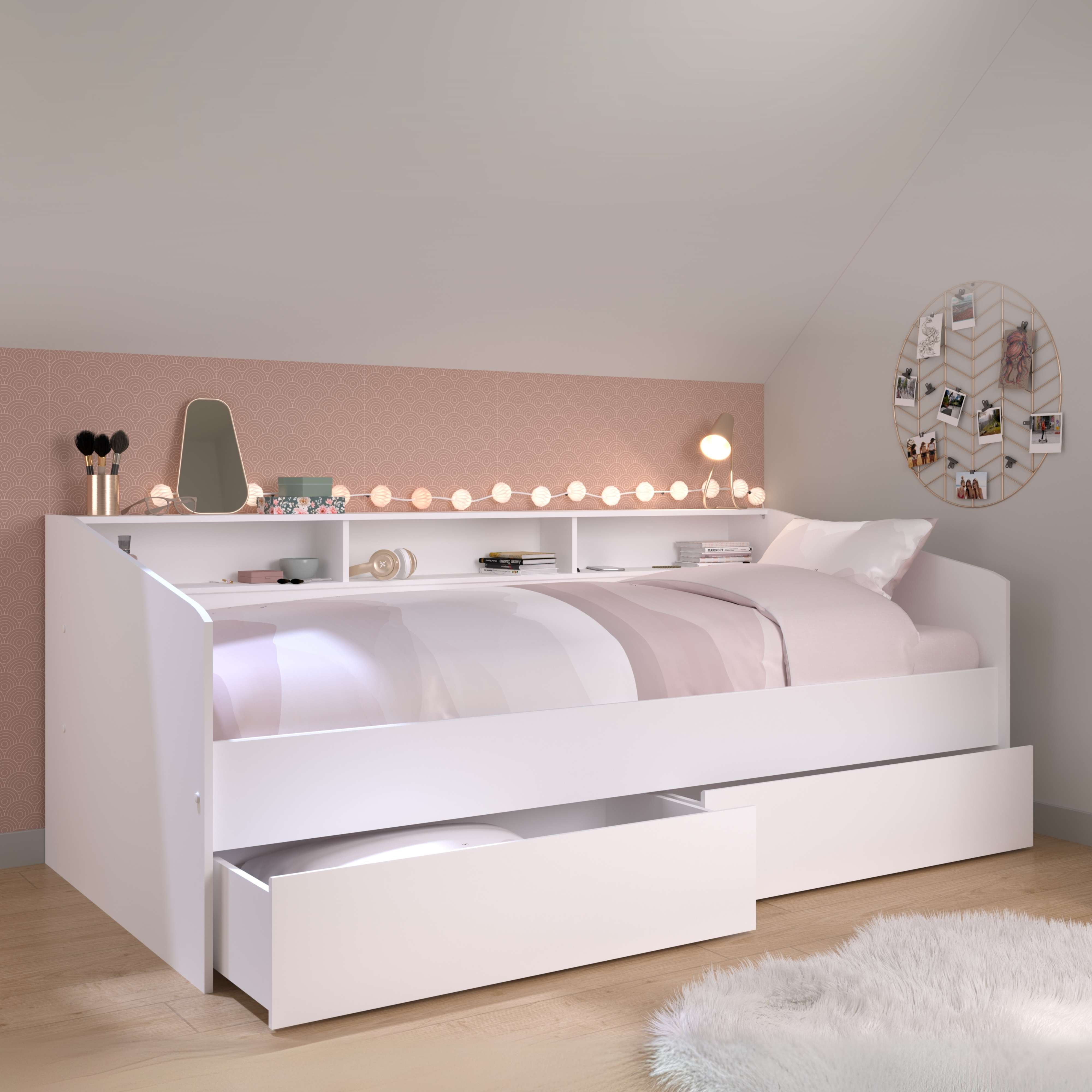 Una cama blanca con cajón, ropa de cama a rayas y estantería.