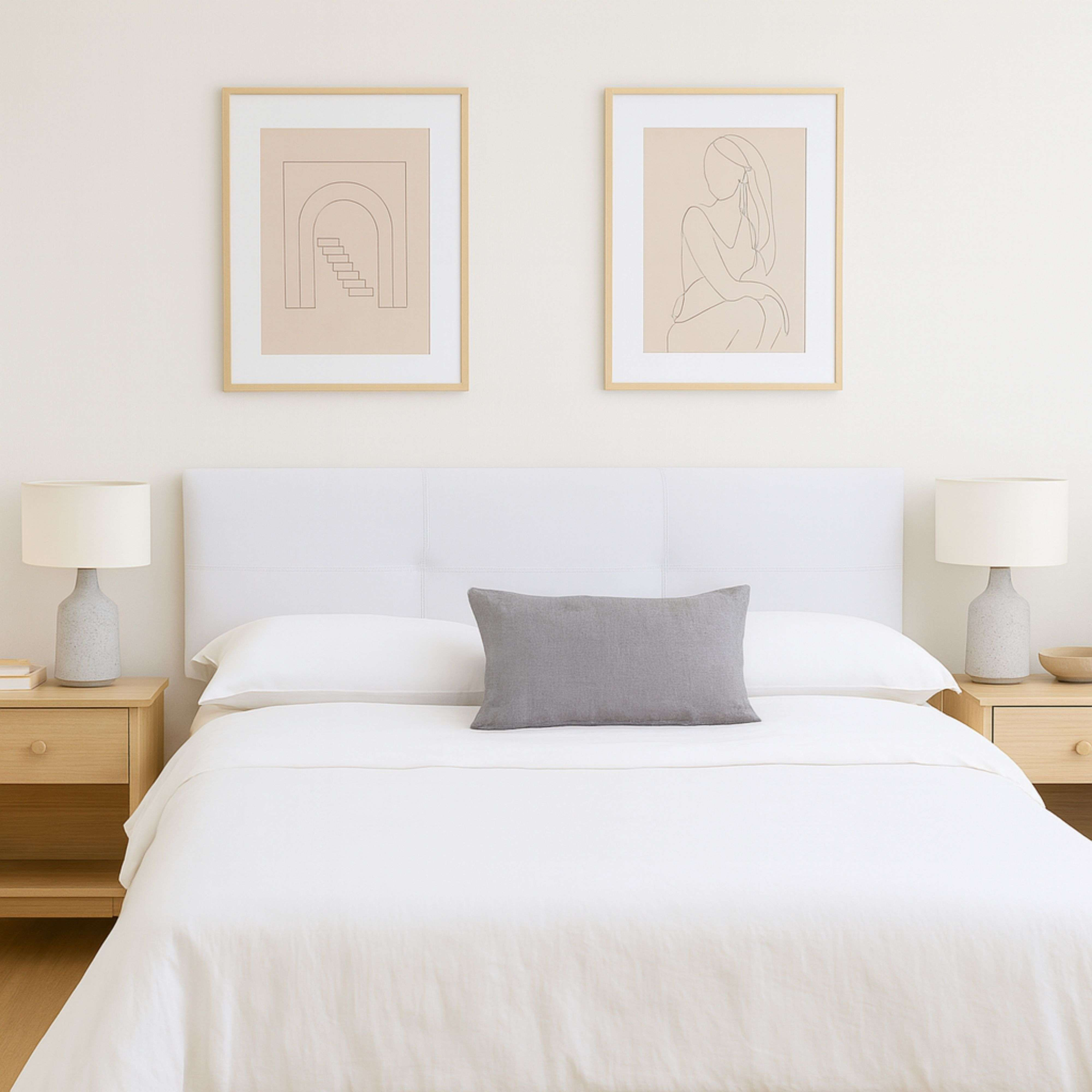 Una cama blanca con dos mesitas de noche, lámparas y dos láminas enmarcadas.