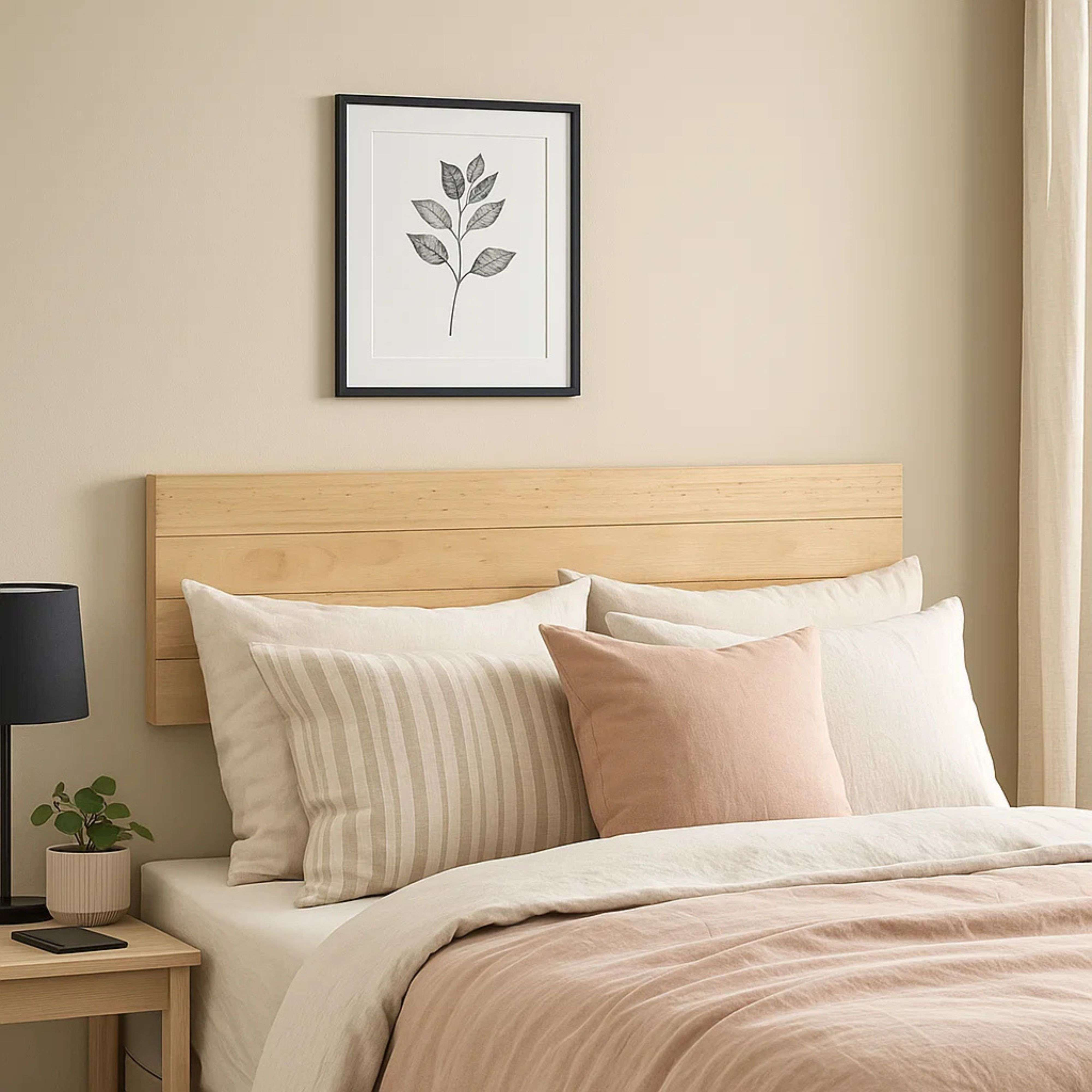 Cama con cabecero de madera clara, ropa de cama neutra y arte de hojas enmarcado.