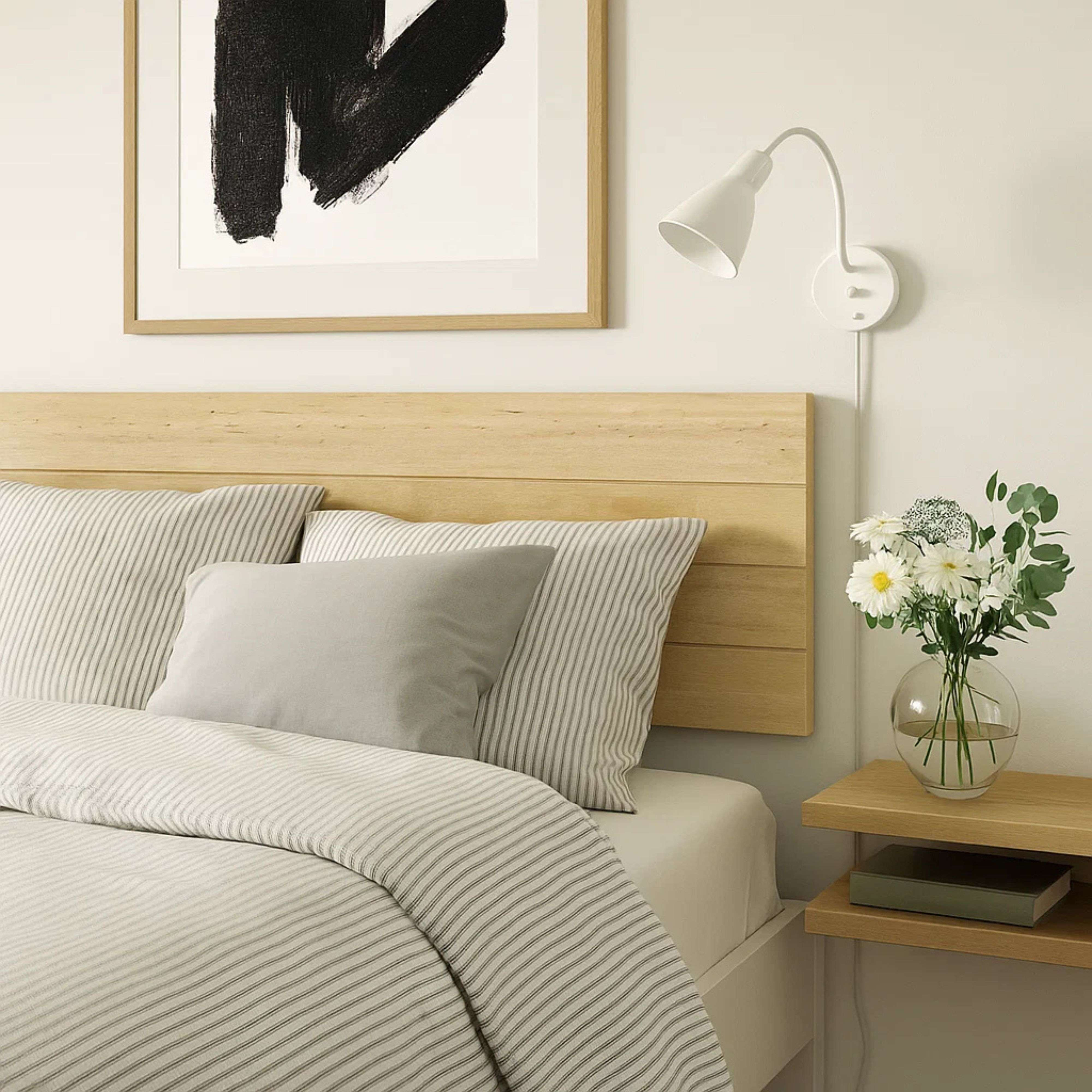 Una cama con ropa de cama a rayas, almohadas y una mesita de noche con flores.