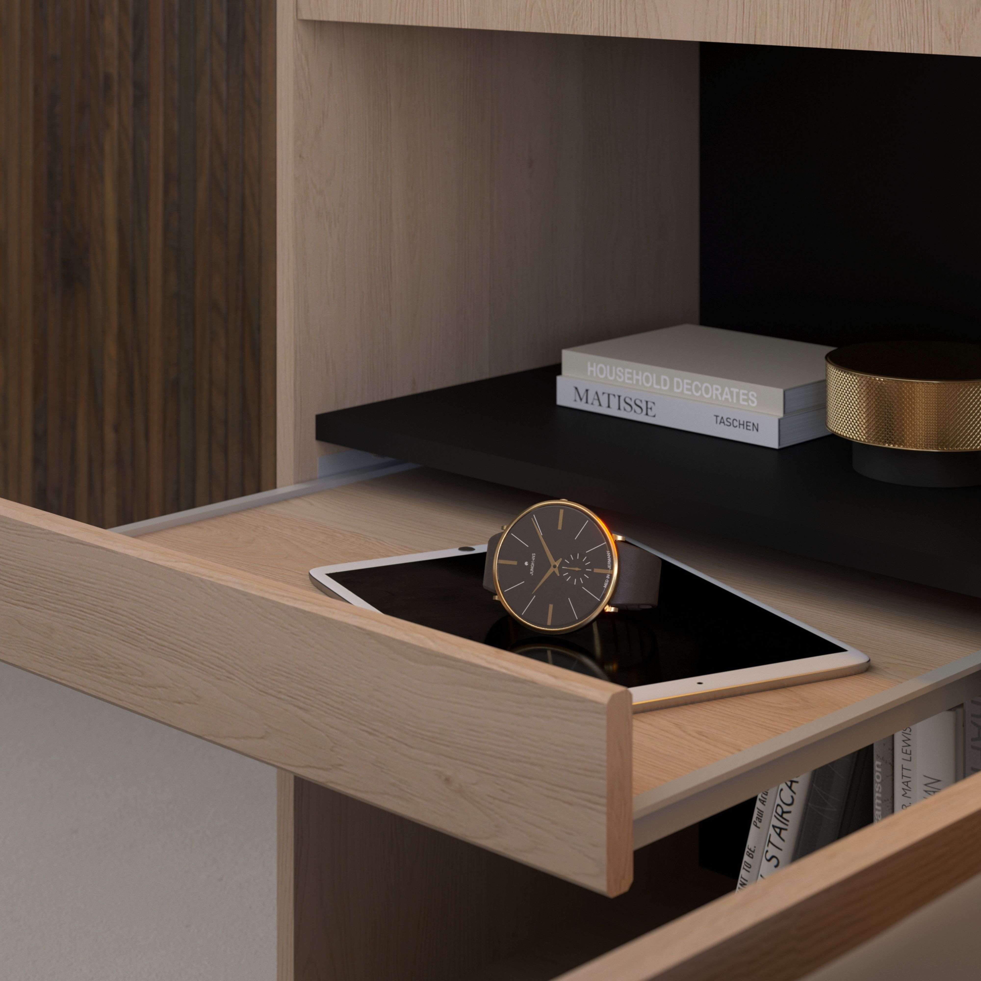 Una tableta y un reloj descansan en un cajón de madera. Libros y decoración en un estante.