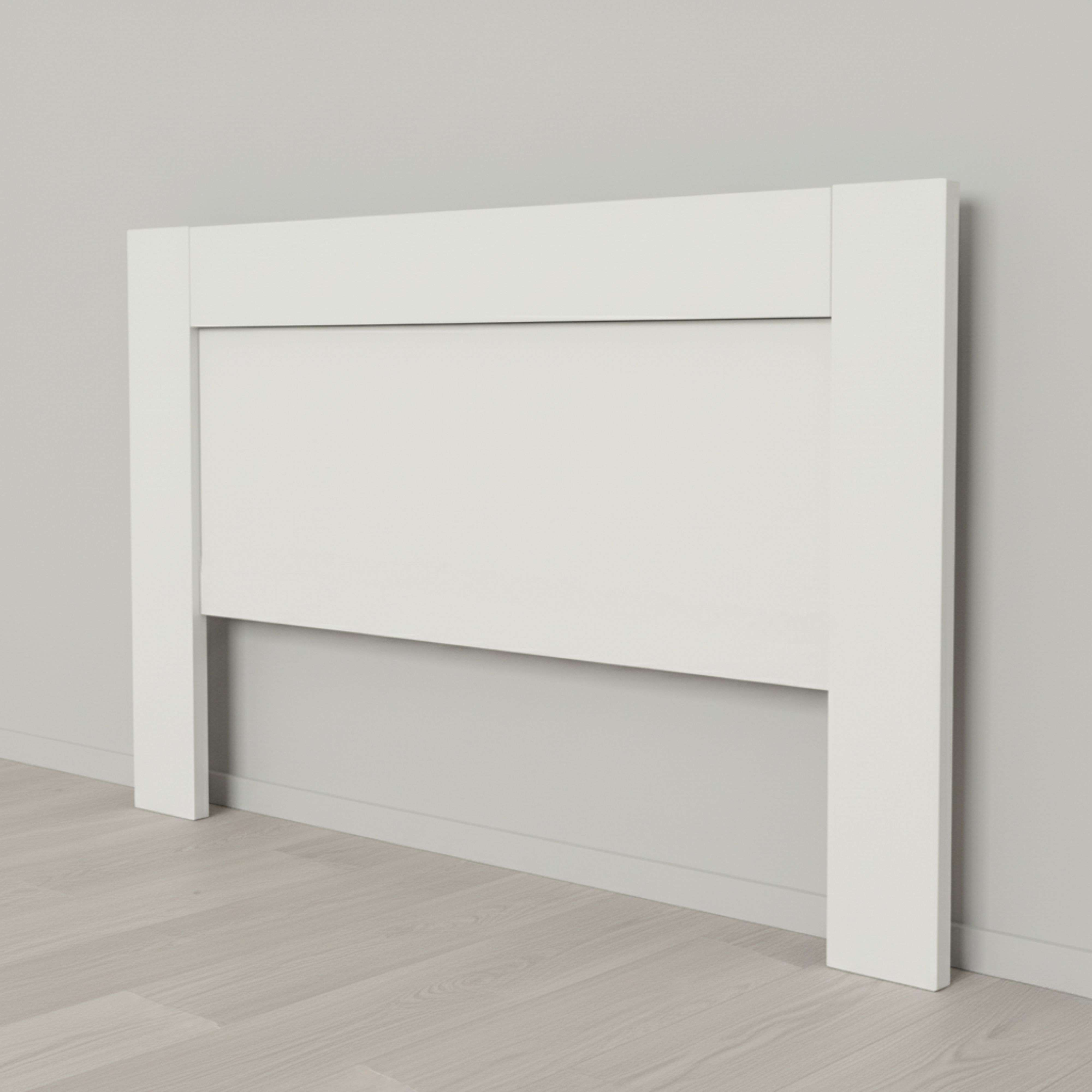 Un cabecero blanco contra una pared gris claro sobre suelo de madera.