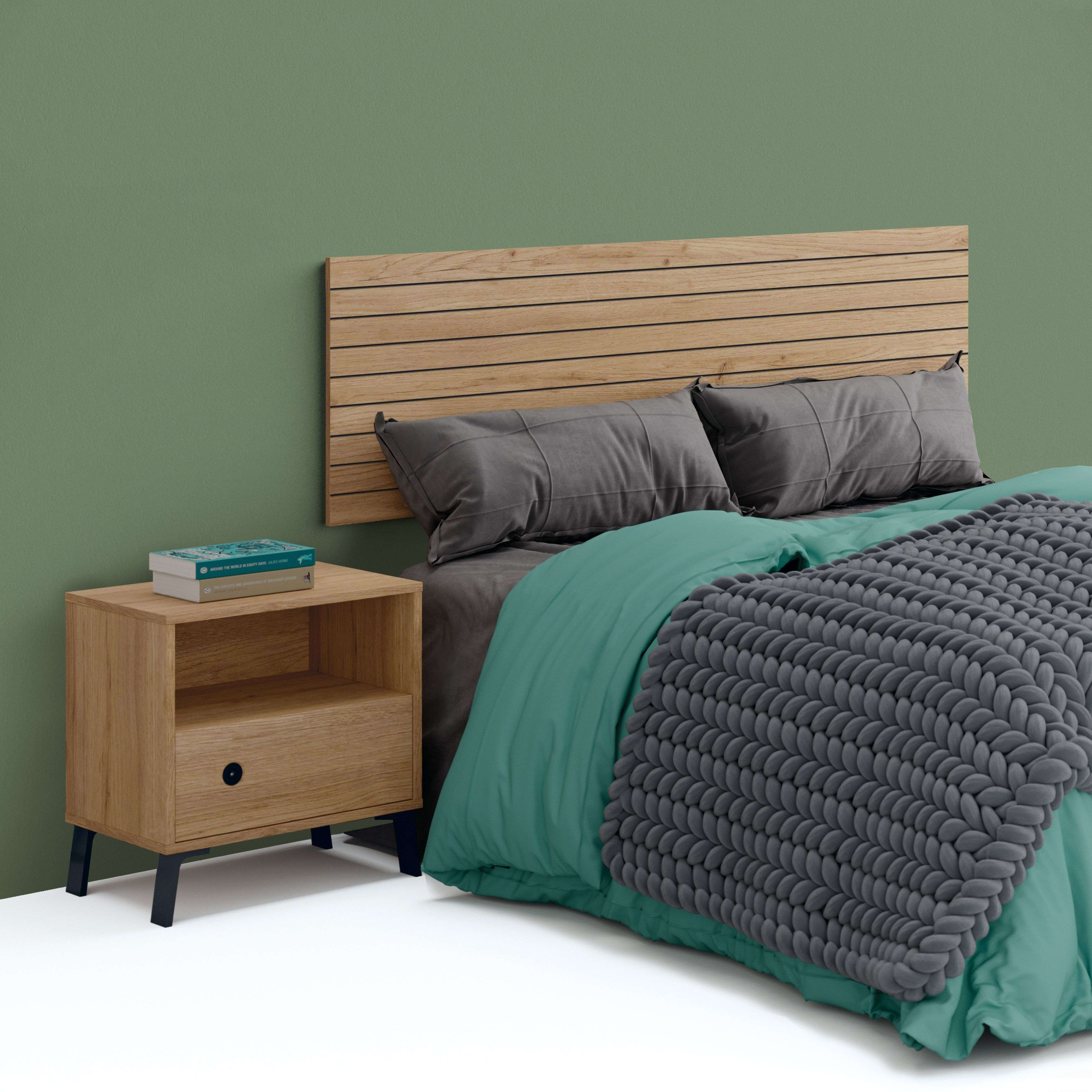 Una mesita de noche de madera con dos libros junto a una cama con ropa de cama verde azulado.