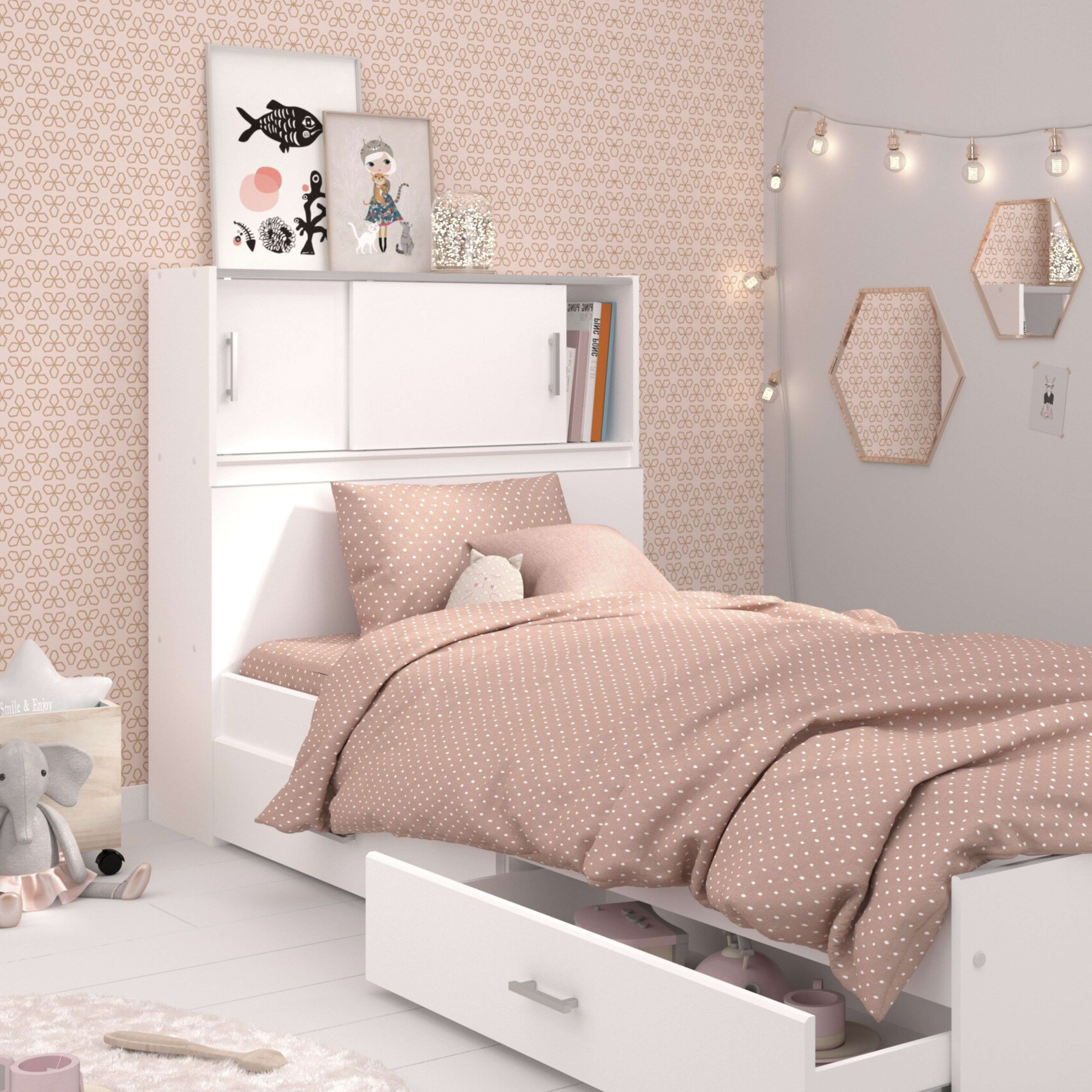 Una cama blanca con ropa de cama de lunares rosas, mesita de noche y juguetes.
