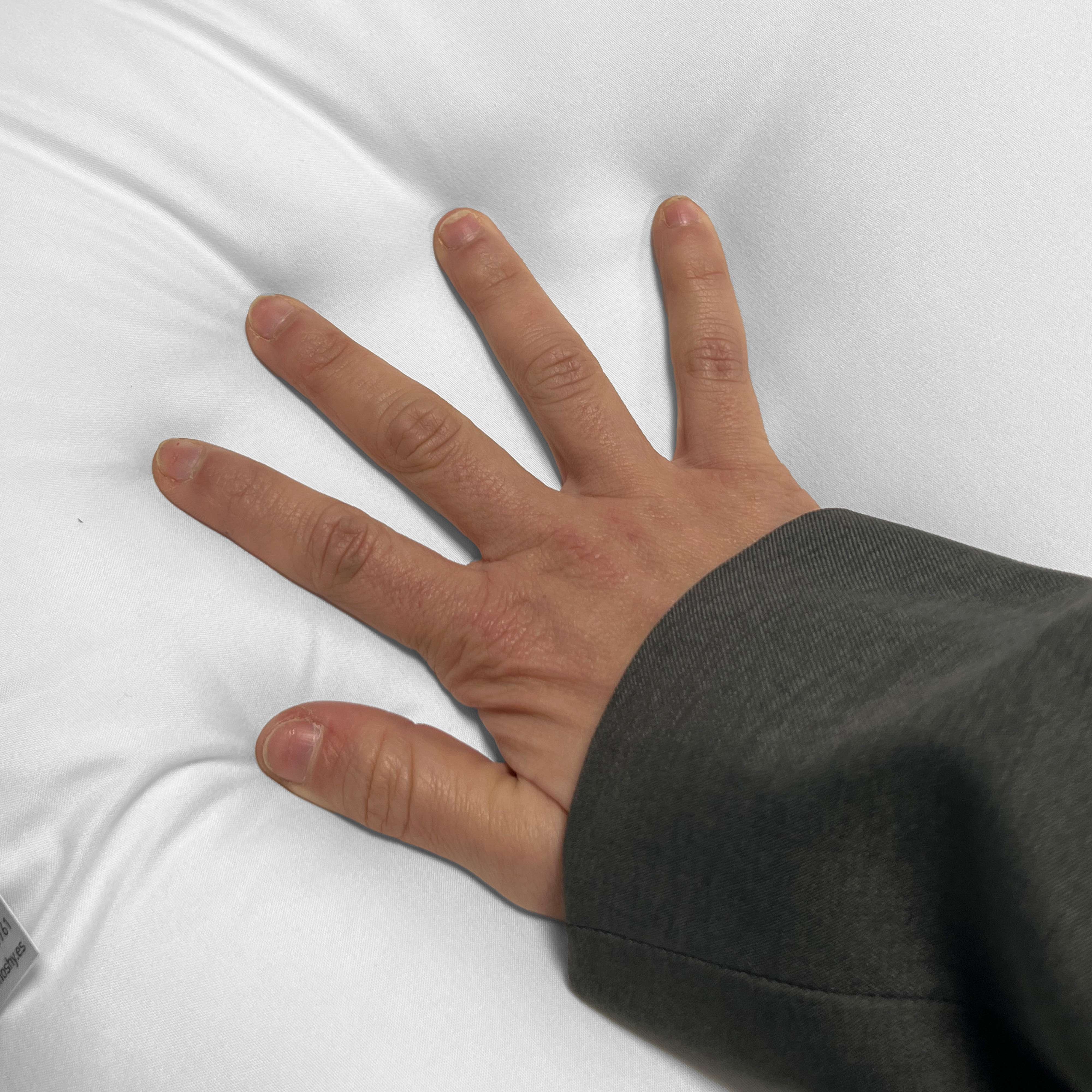 Una mano con los dedos extendidos descansa sobre una superficie blanca y texturizada. Se ve una prenda gris oscura.