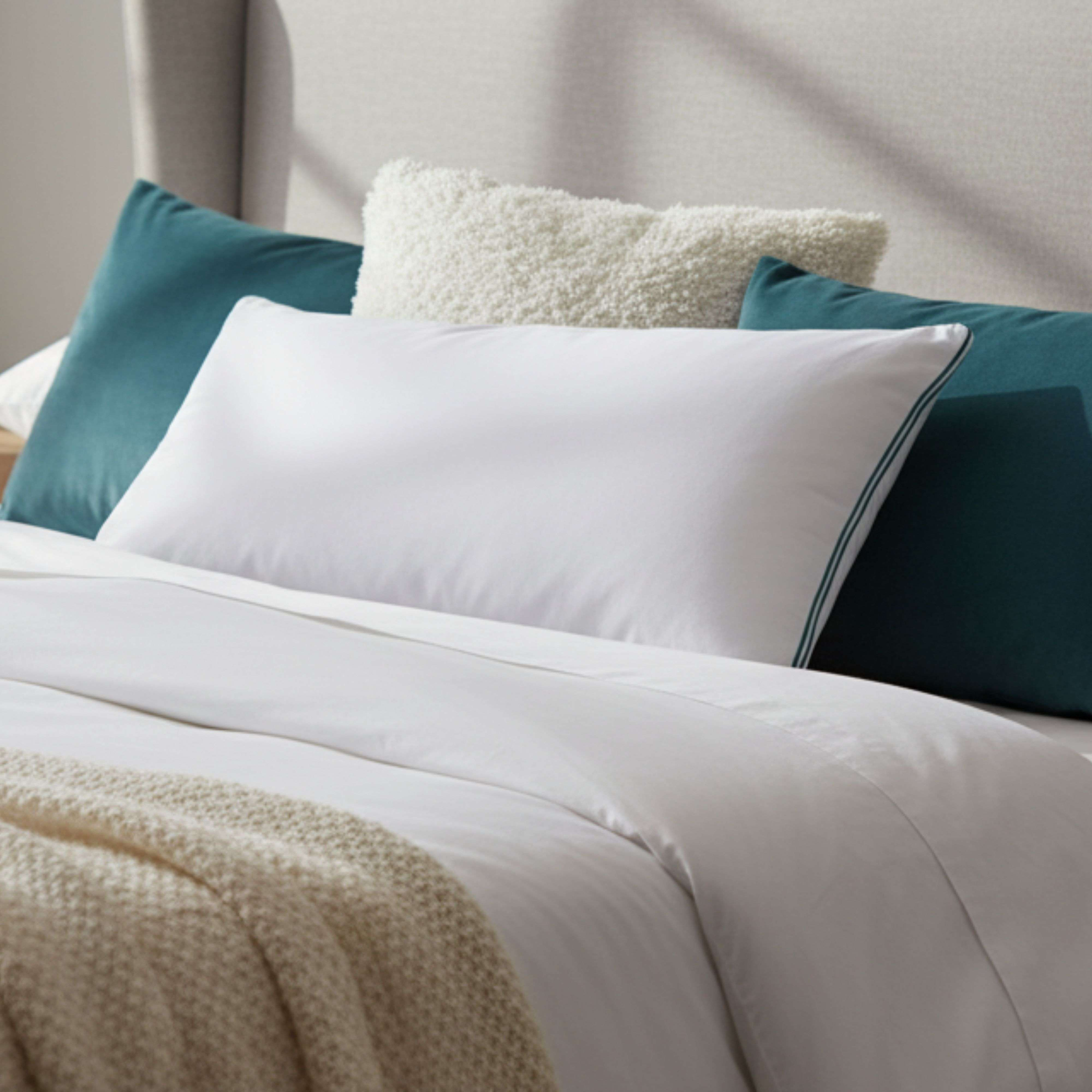 Una almohada blanca con ribete verde descansa sobre una cama con almohadas azules y esponjosas.