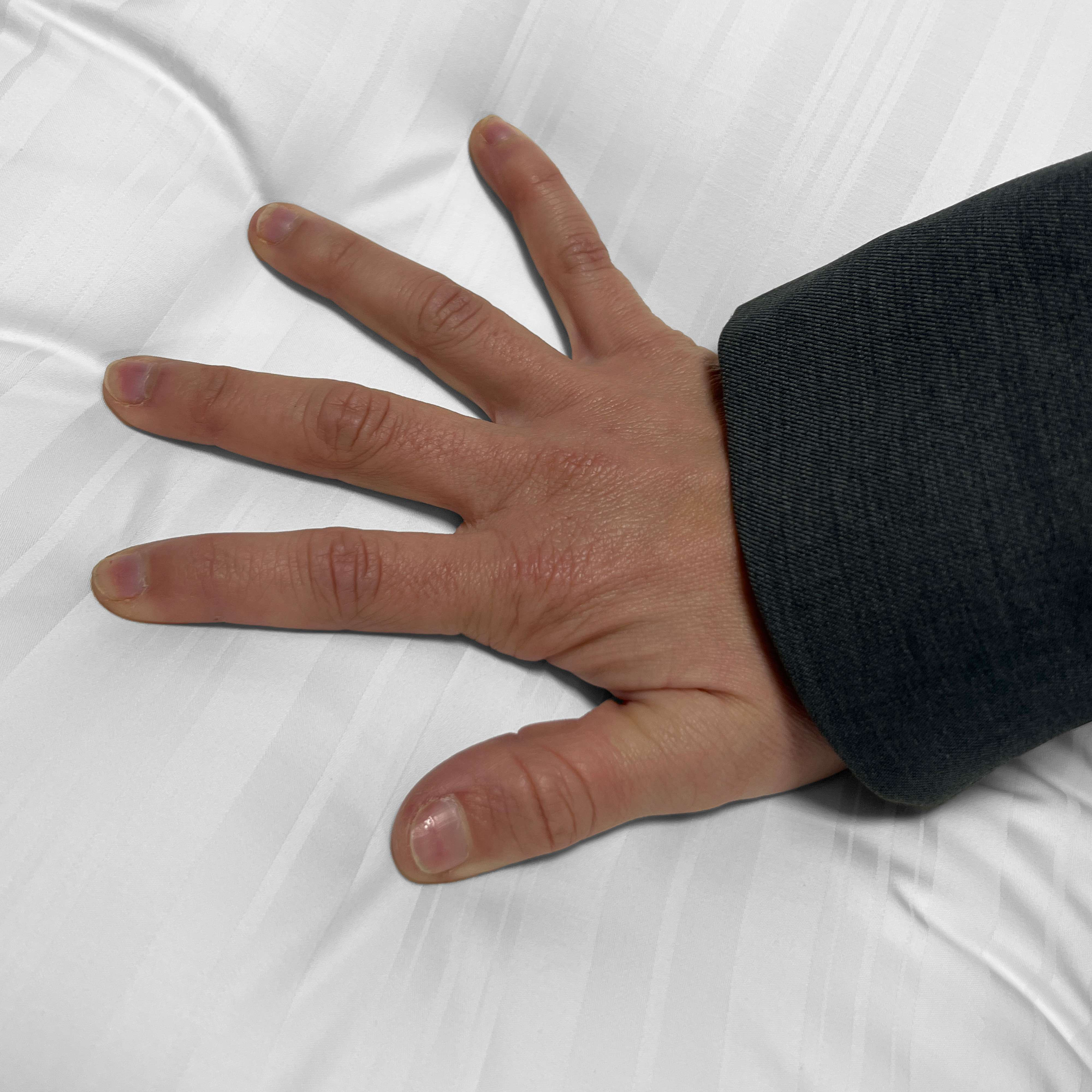 Una mano presiona una superficie suave, blanca y rayada. Se ve ropa oscura.