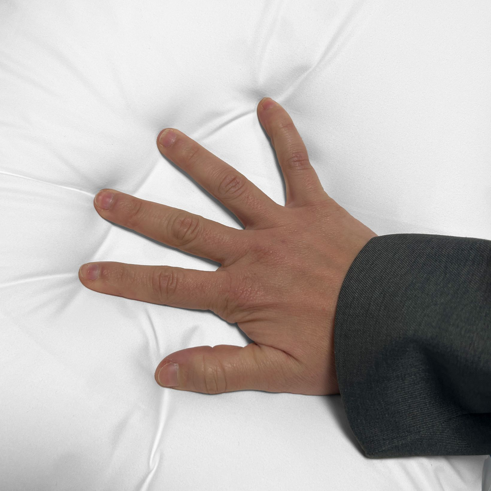 Una mano con una chaqueta gris presiona sobre un material blanco y suave.