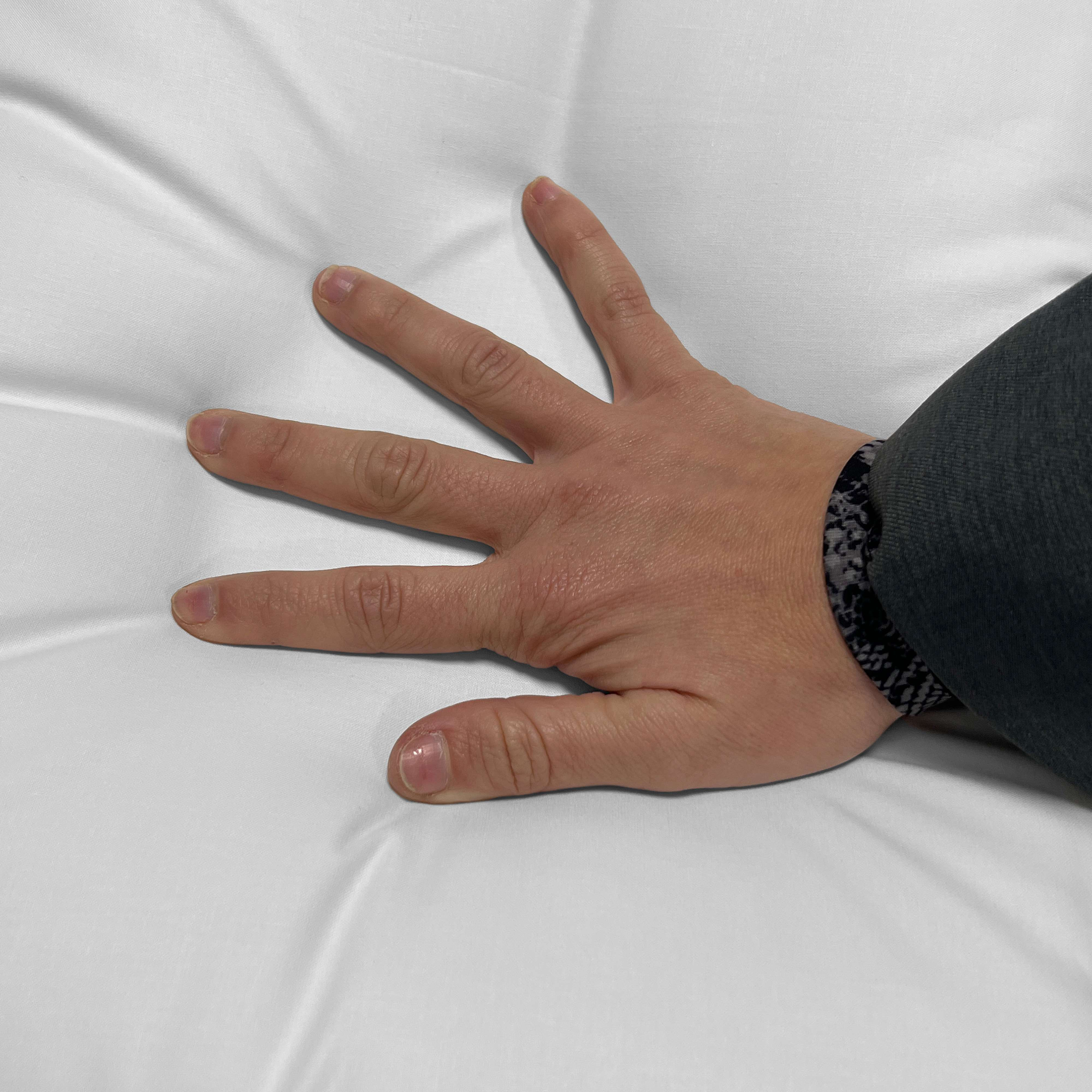 Una mano presiona una tela blanca y arrugada. Se ve una pulsera.