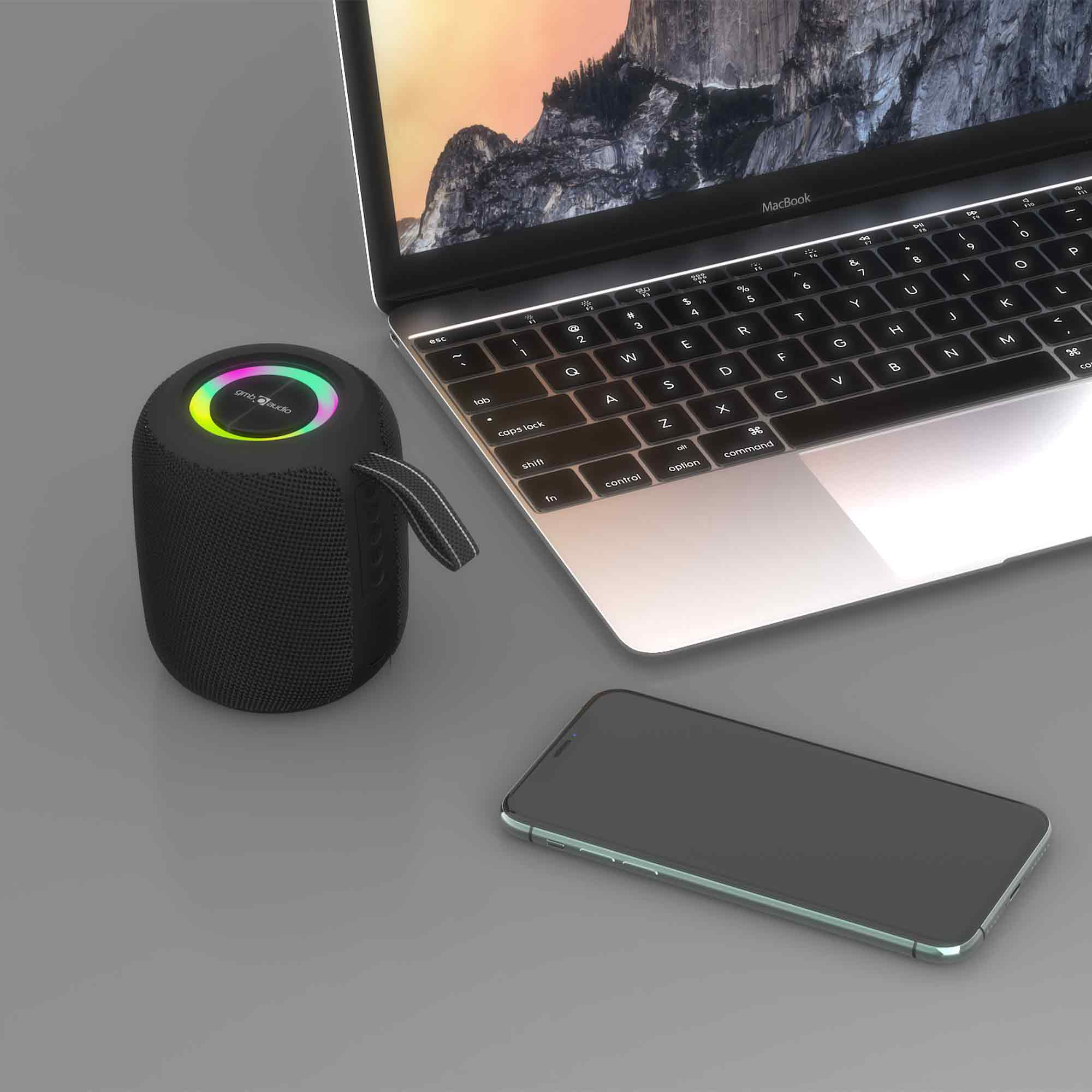 Een zwarte draagbare luidspreker, MacBook en iPhone op een grijze ondergrond.