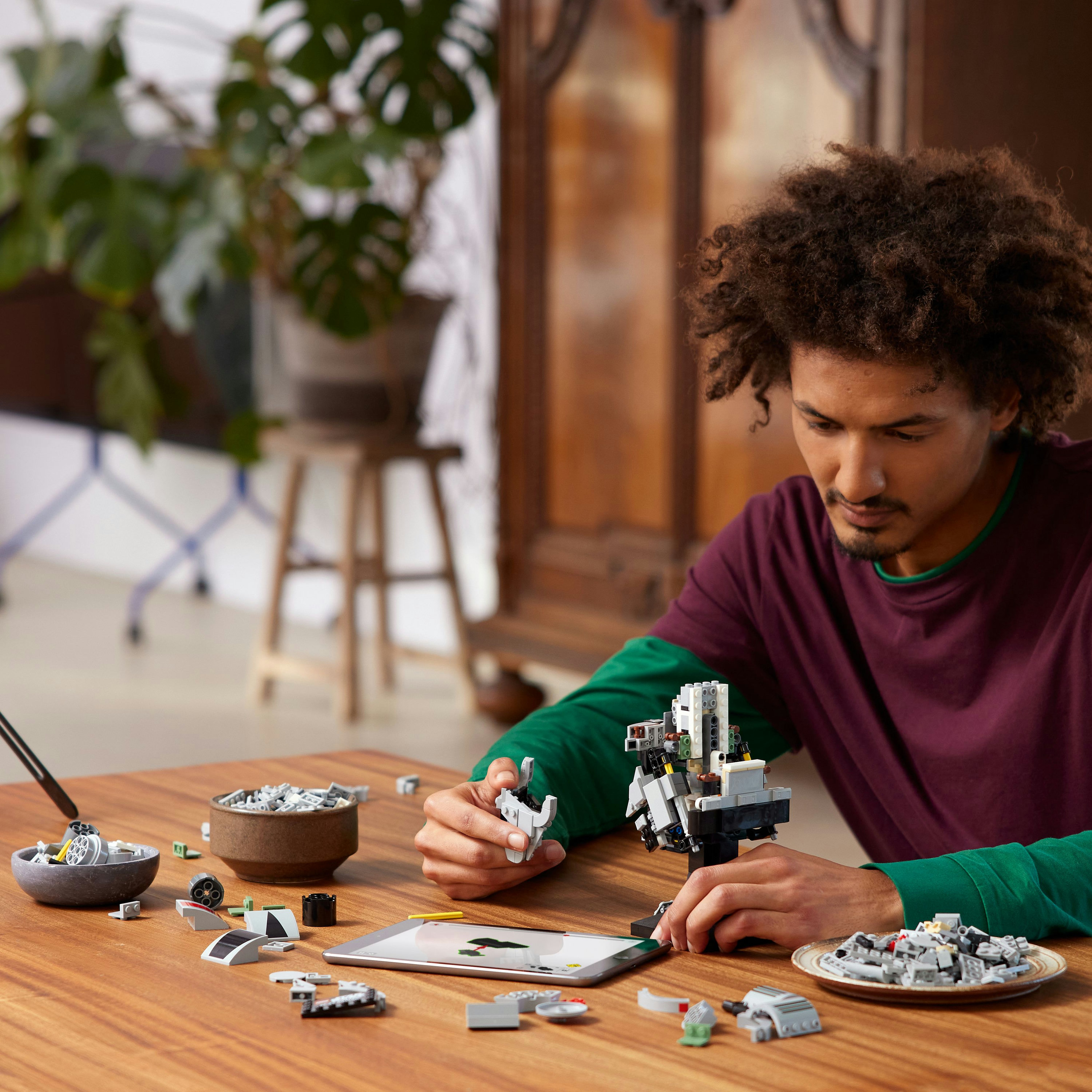 Un homme construit un robot avec des pièces Lego, instructions sur une tablette.