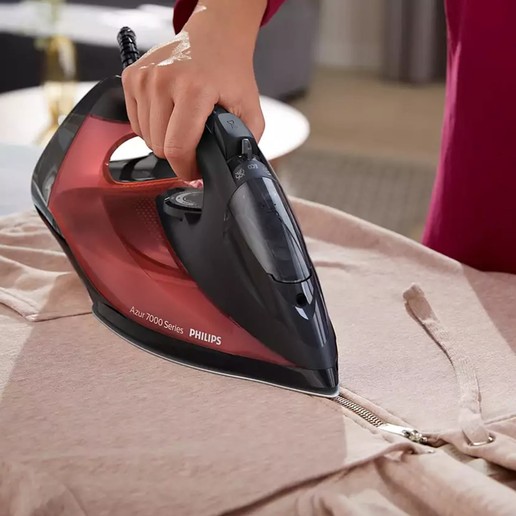El, kırmızı Philips ütü ile pembe bir kapüşonluyu ütülüyor.