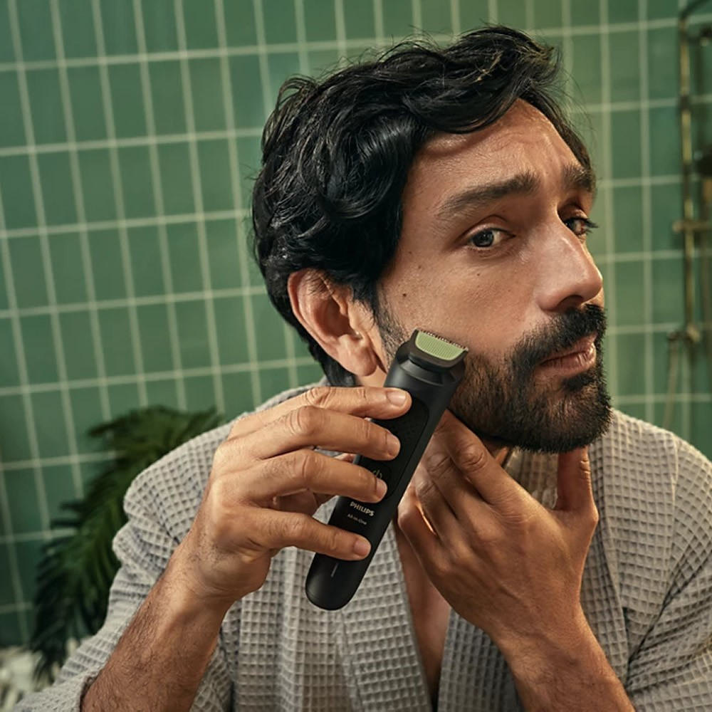 BorInanlı adam, yeşil fayans duvara karşı Philips düzelticiyle sakalını tıraş ediyor.