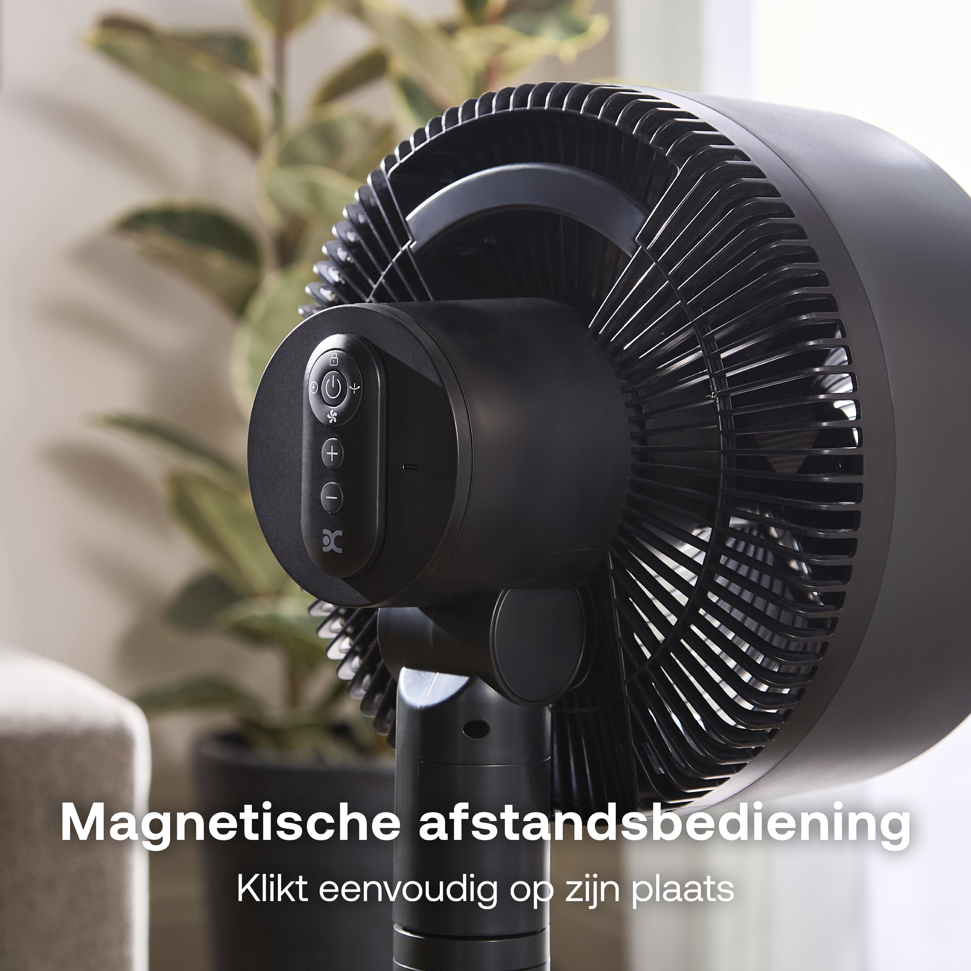 Een zwarte ventilator met bedieningsknoppen en gebladerte op de achtergrond.