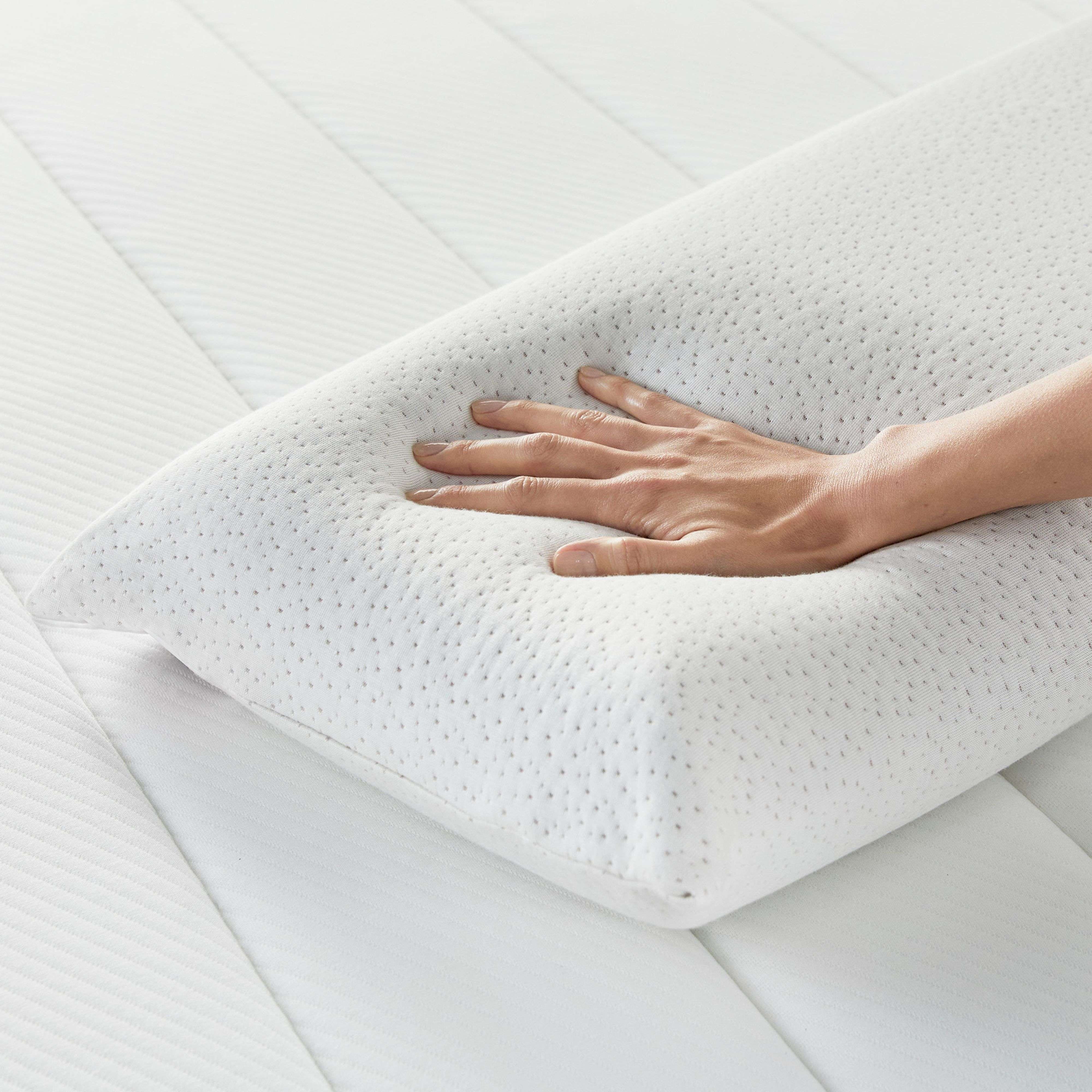 Una mano presiona un cojín blanco sobre un colchón.