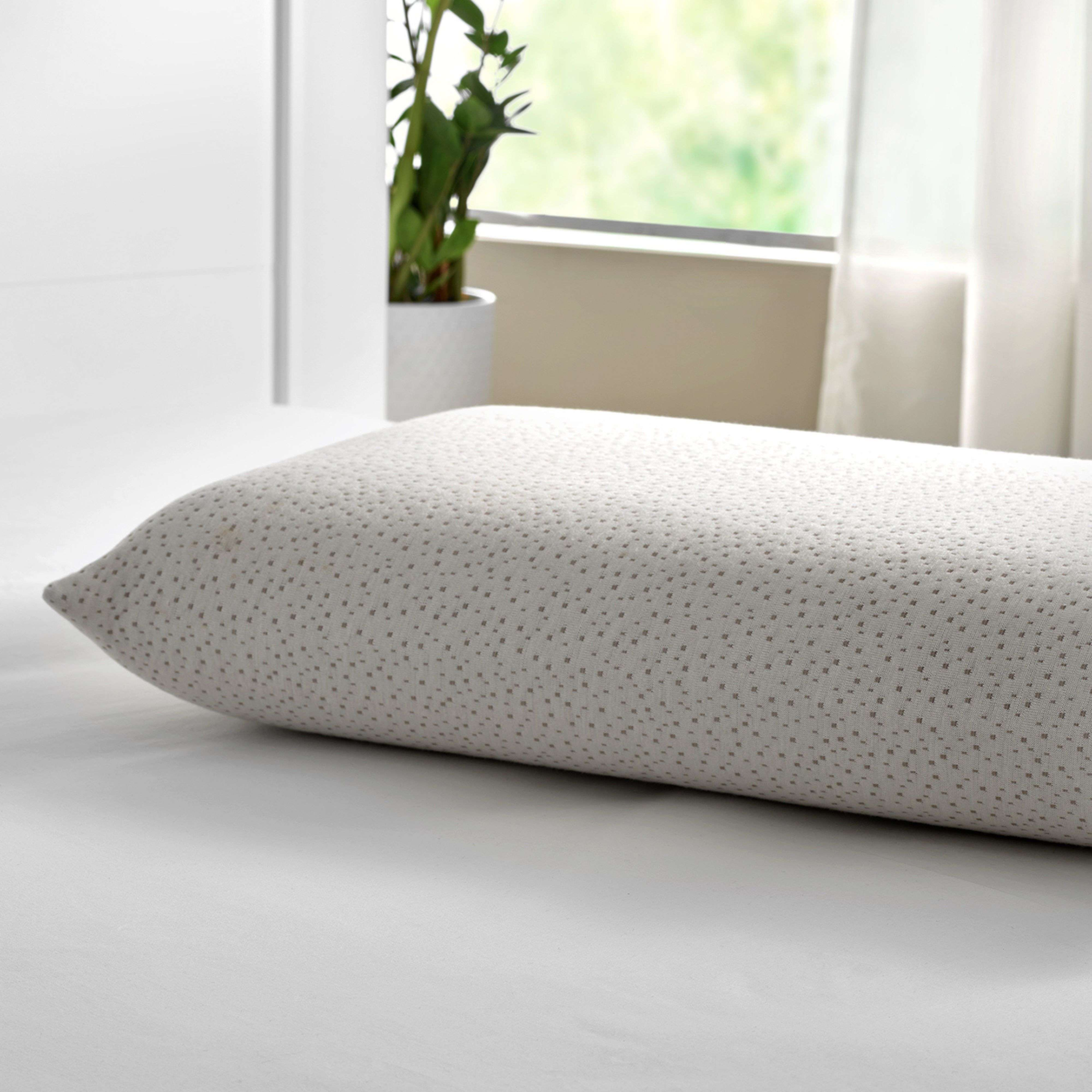 Una almohada de color claro con patrón de puntos descansa sobre una cama blanca.