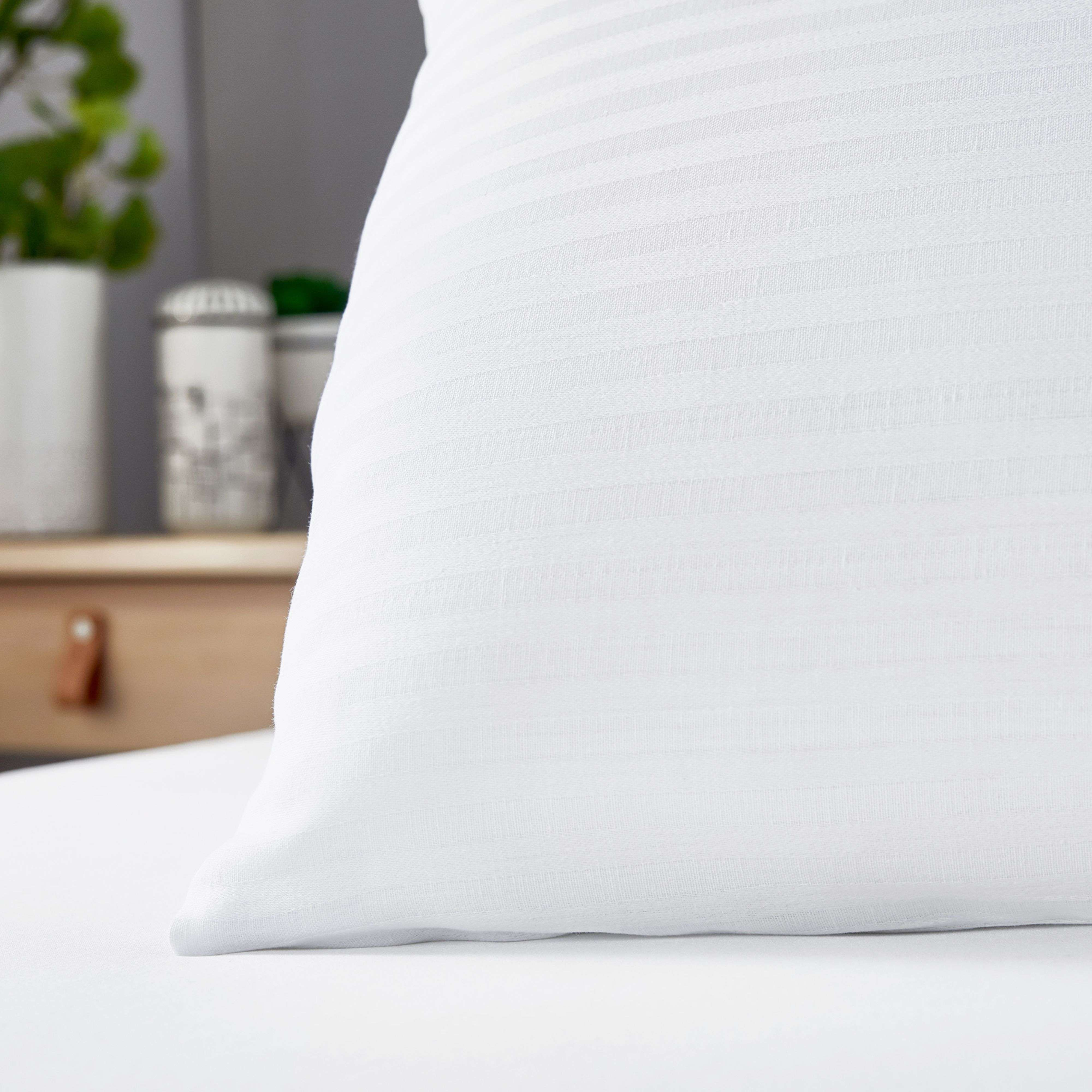 Una almohada blanca a rayas descansa sobre una cama. Plantas y decoración al fondo.