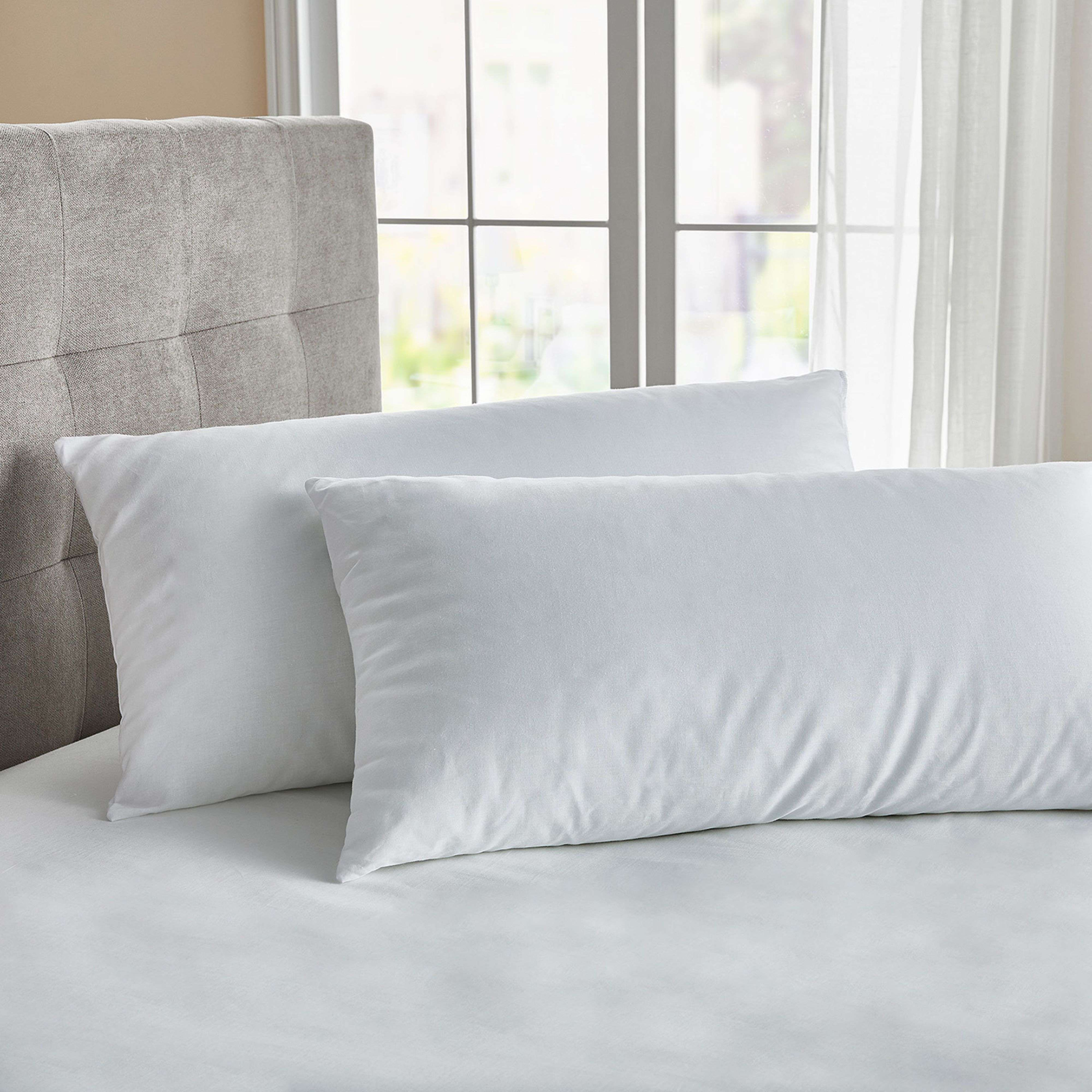 Dos almohadas blancas descansan sobre una cama con cabecero gris.