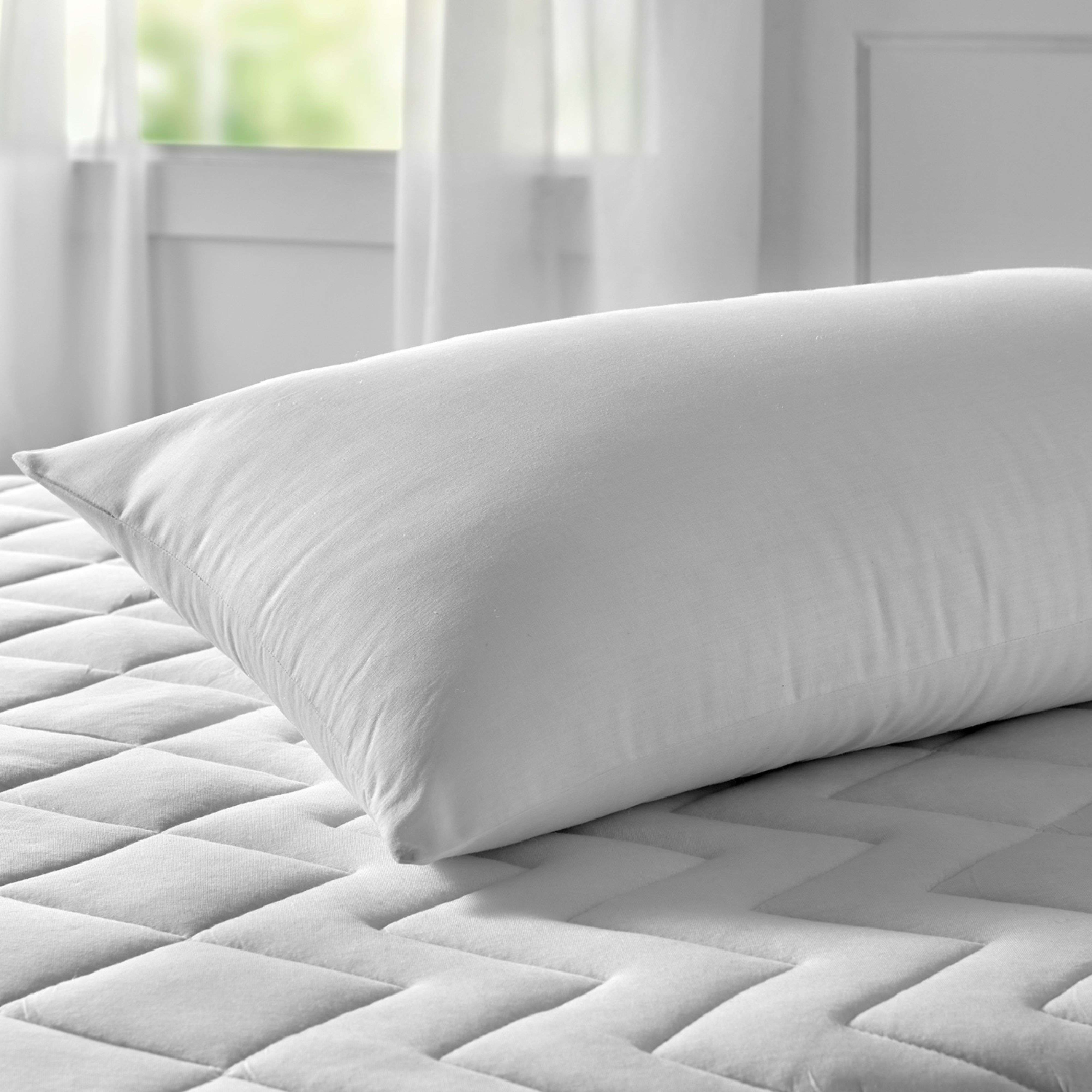 Una almohada blanca descansa sobre un colchón blanco acolchado junto a una ventana.