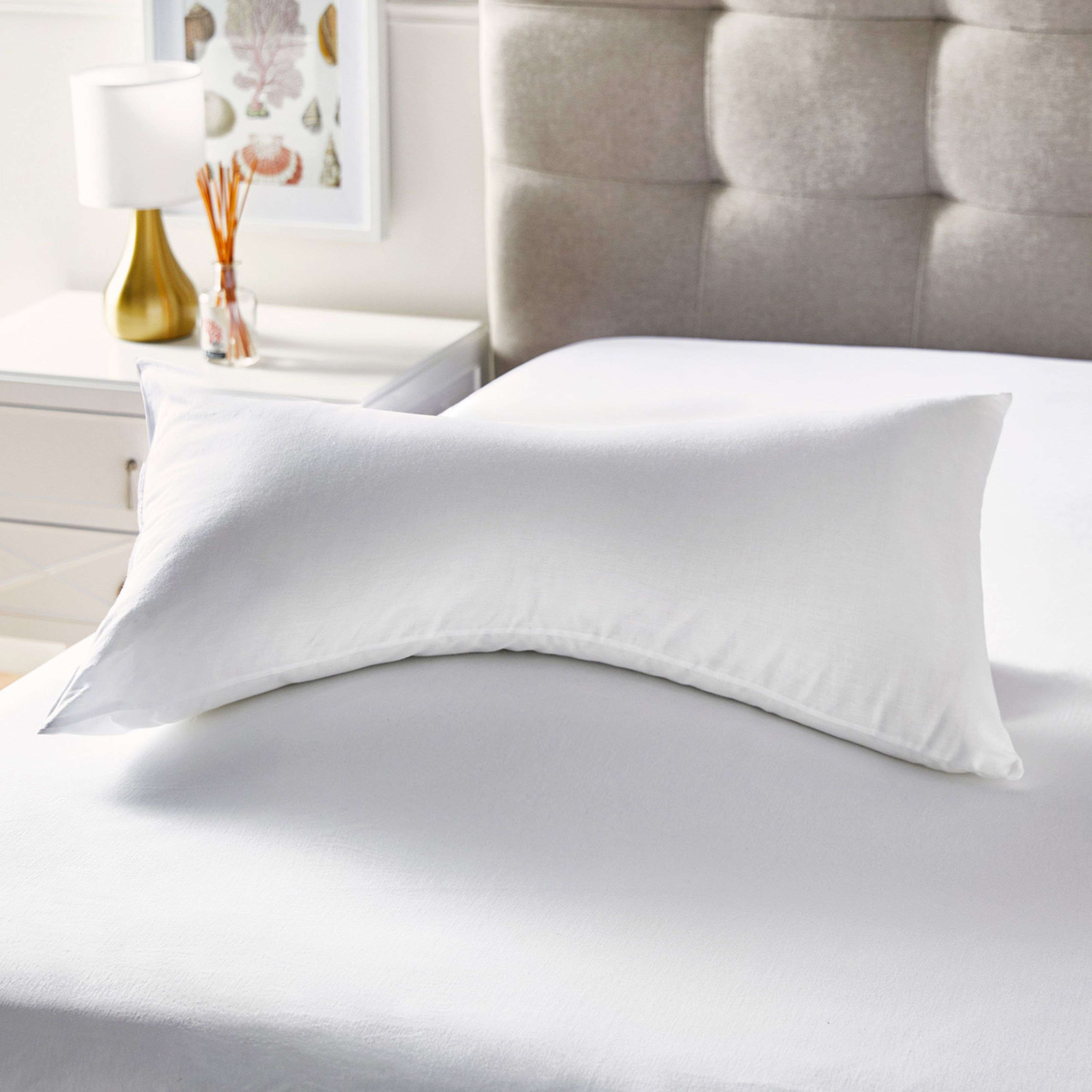 Una almohada blanca descansa sobre una cama blanca con cabecero tapizado al fondo.