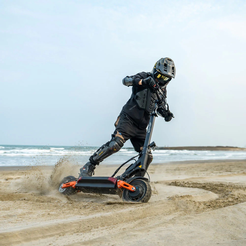 Persona con equipo de protección monta un patinete eléctrico en playa de arena.