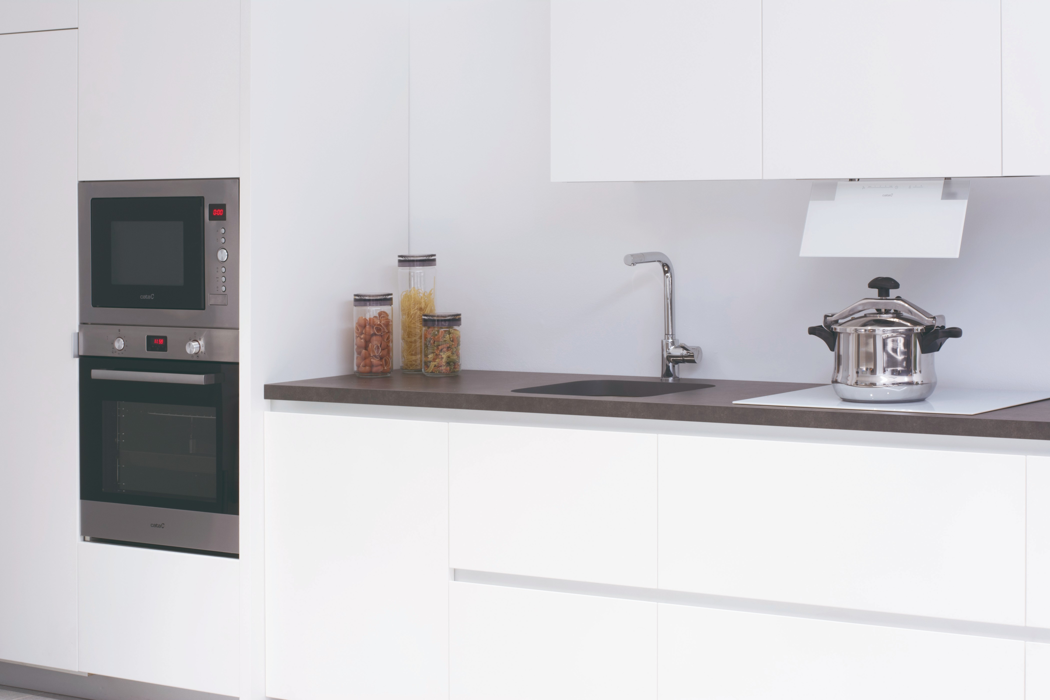 Moderna cocina blanca con microondas, horno, fregadero, campana y olla a presión.