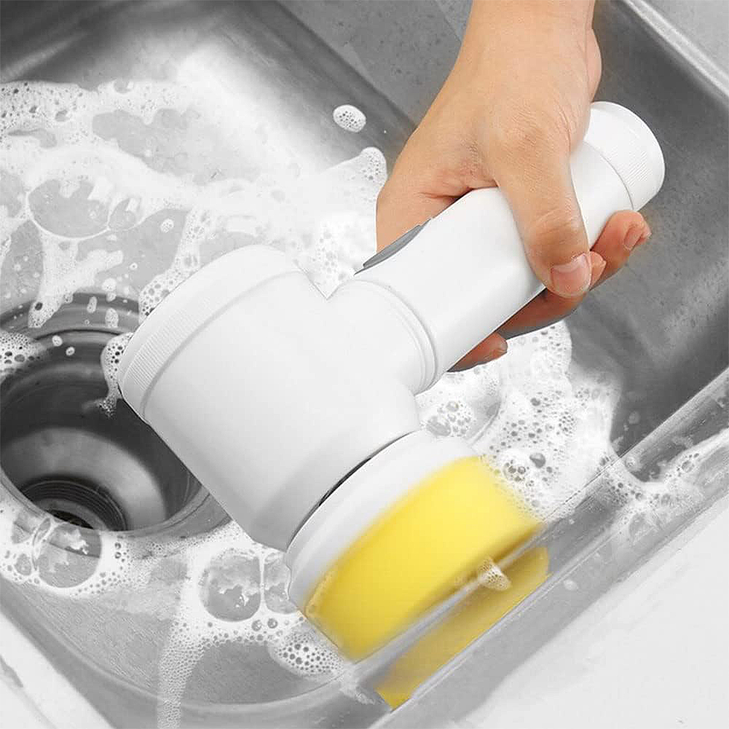 Una mano sostiene un cepillo eléctrico blanco con esponja amarilla en un fregadero.