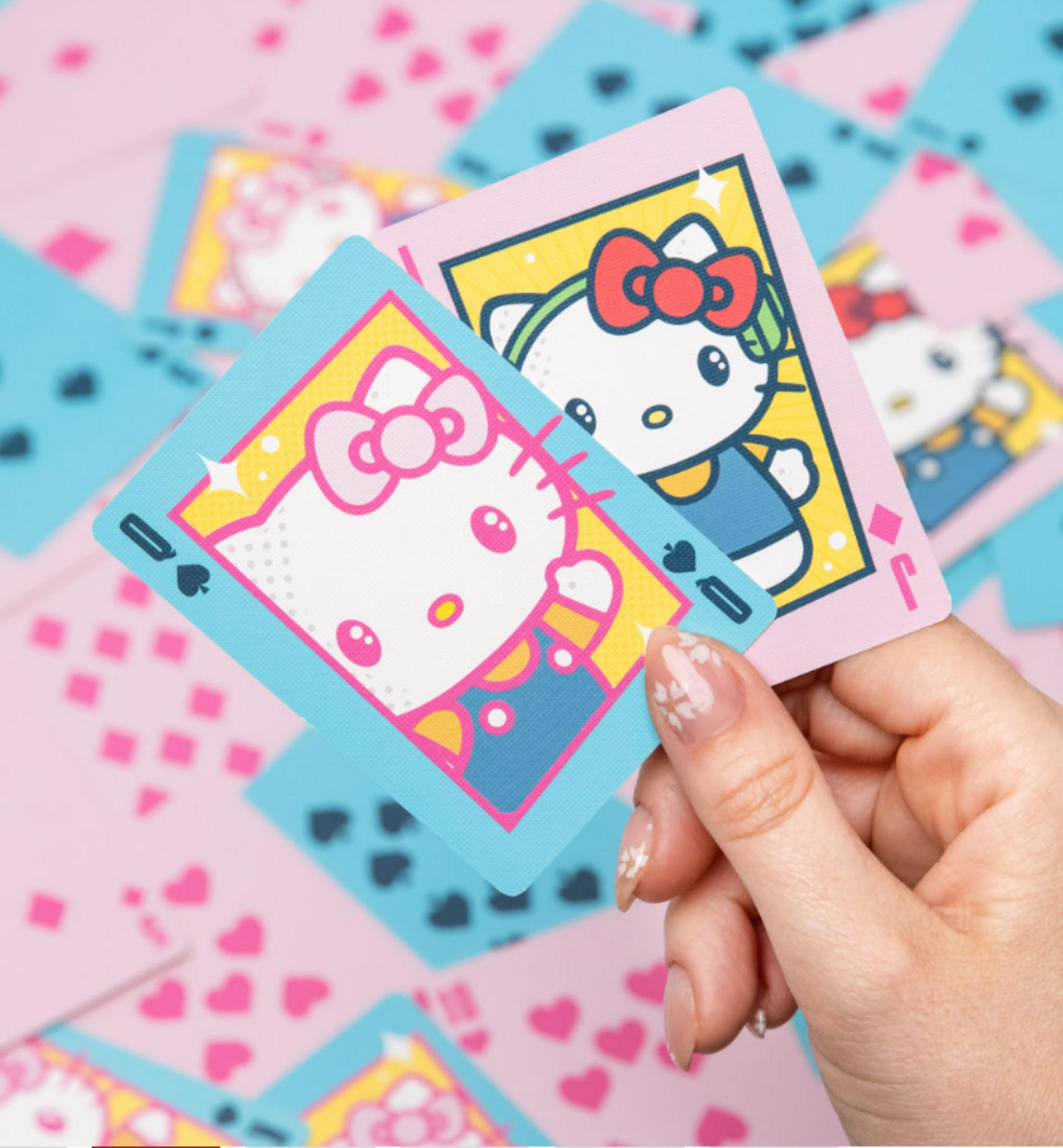 Une main tenant deux cartes à jouer mettant en vedette Hello Kitty et des motifs.