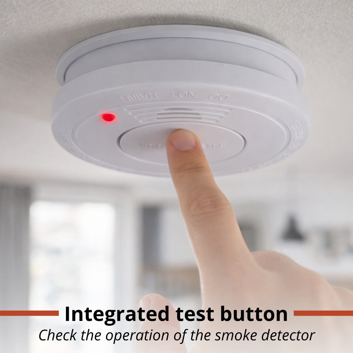 Un doigt appuie sur le bouton test d'un détecteur de fumée blanc au plafond avec une lumière rouge.