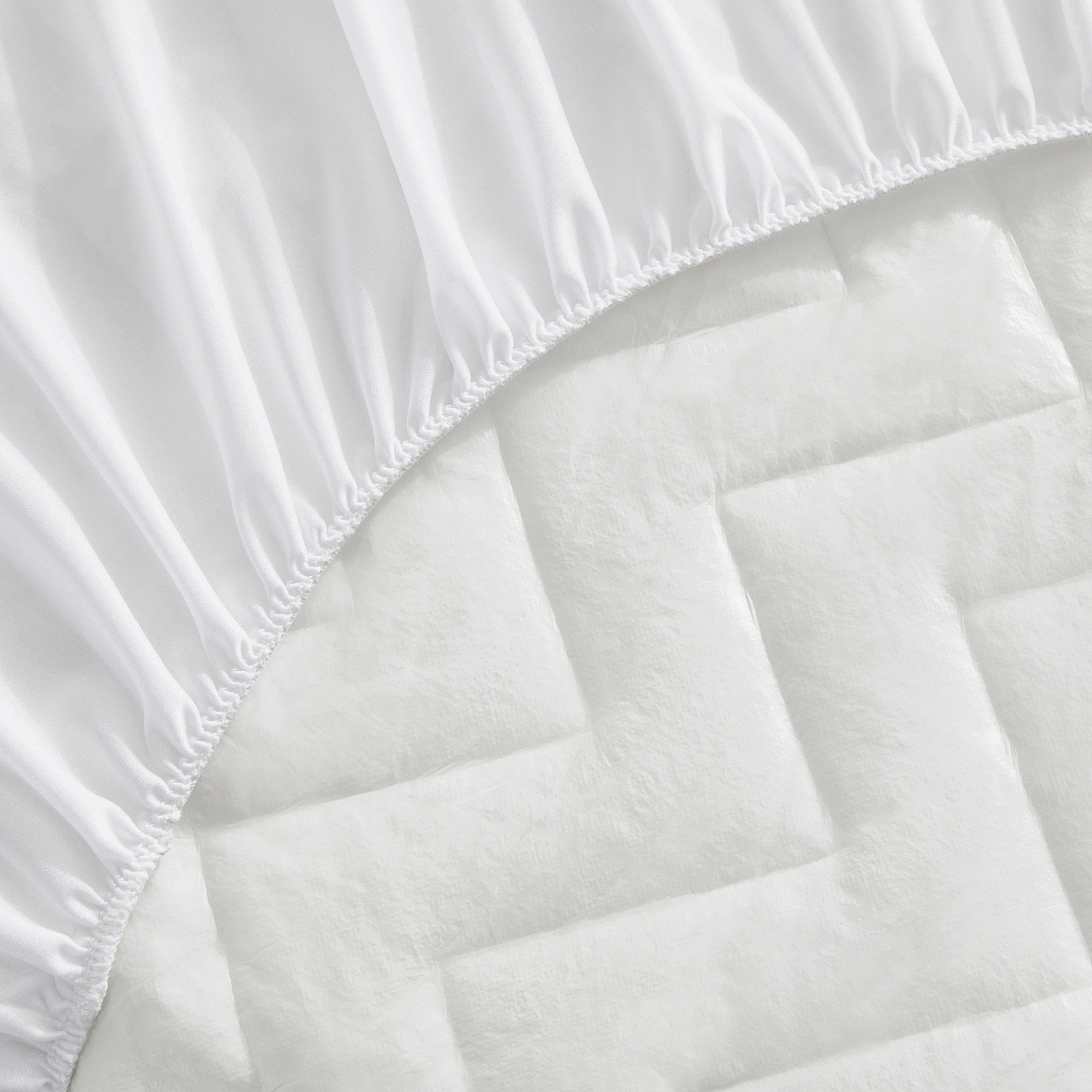 Una sábana bajera blanca con elástico sobre un cubrecolchón acolchado.