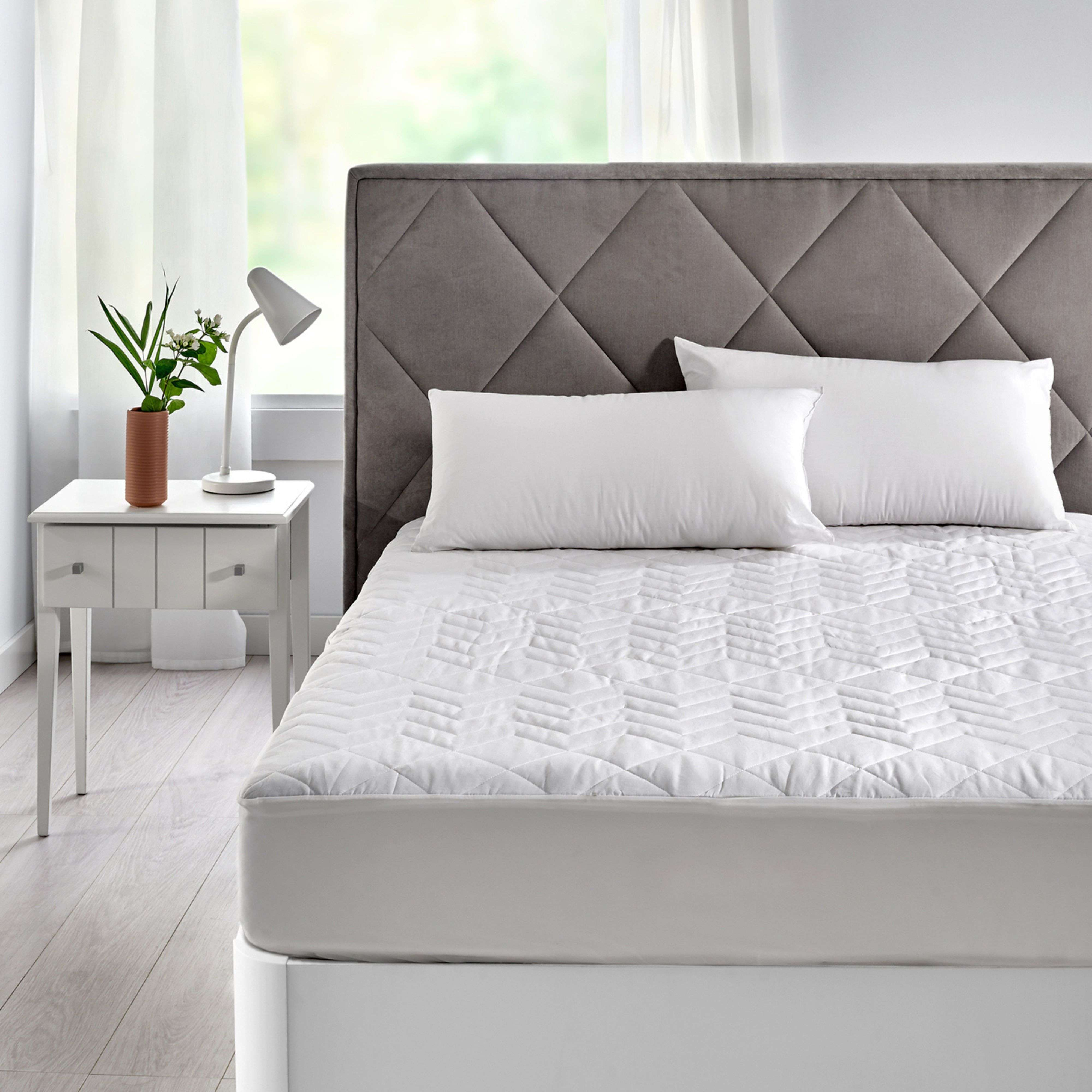 Una cama con cabecero gris acolchado, dos almohadas blancas y una colcha blanca acolchada.