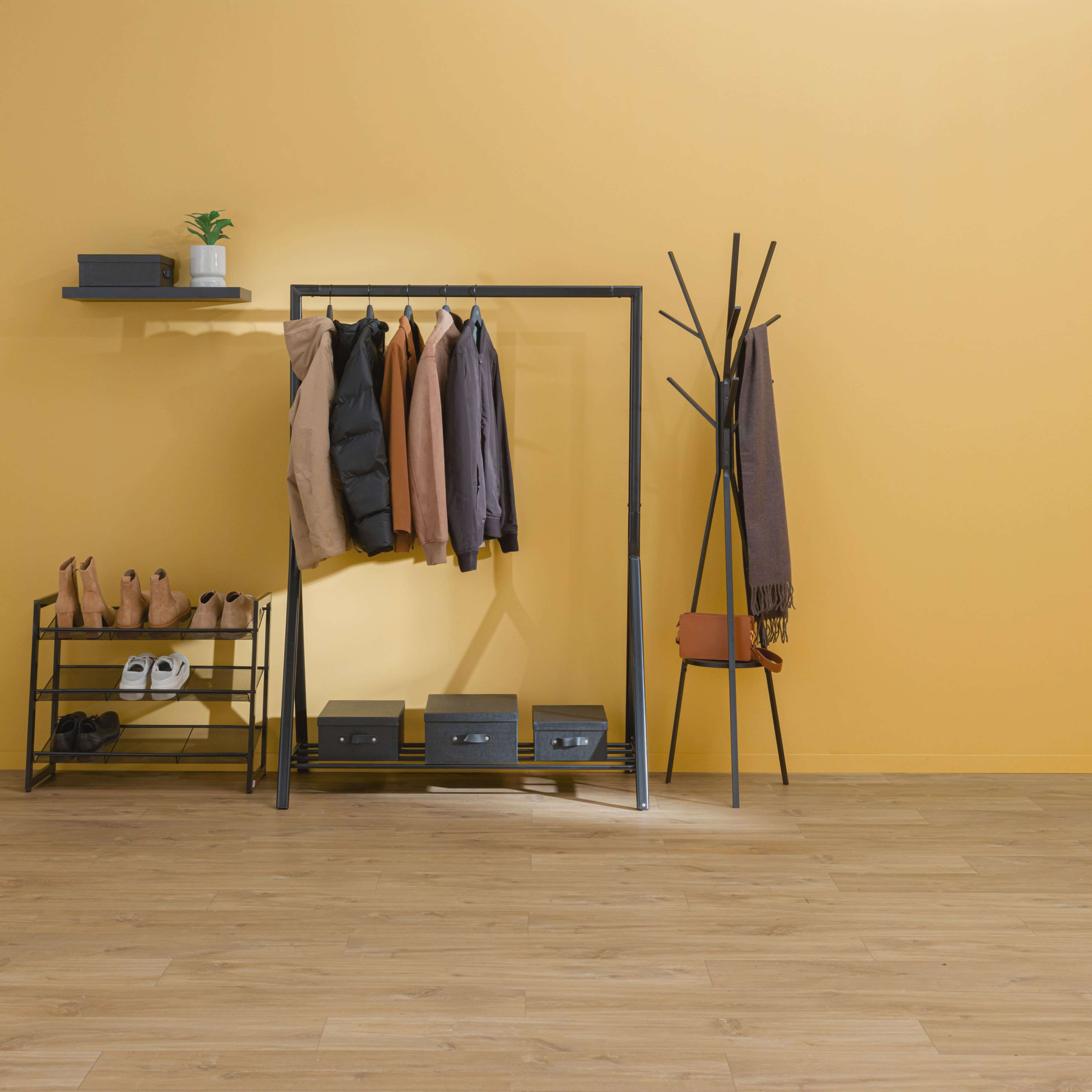 Pasillo con perchero, zapatero, cajas y decoración frente a pared amarilla.