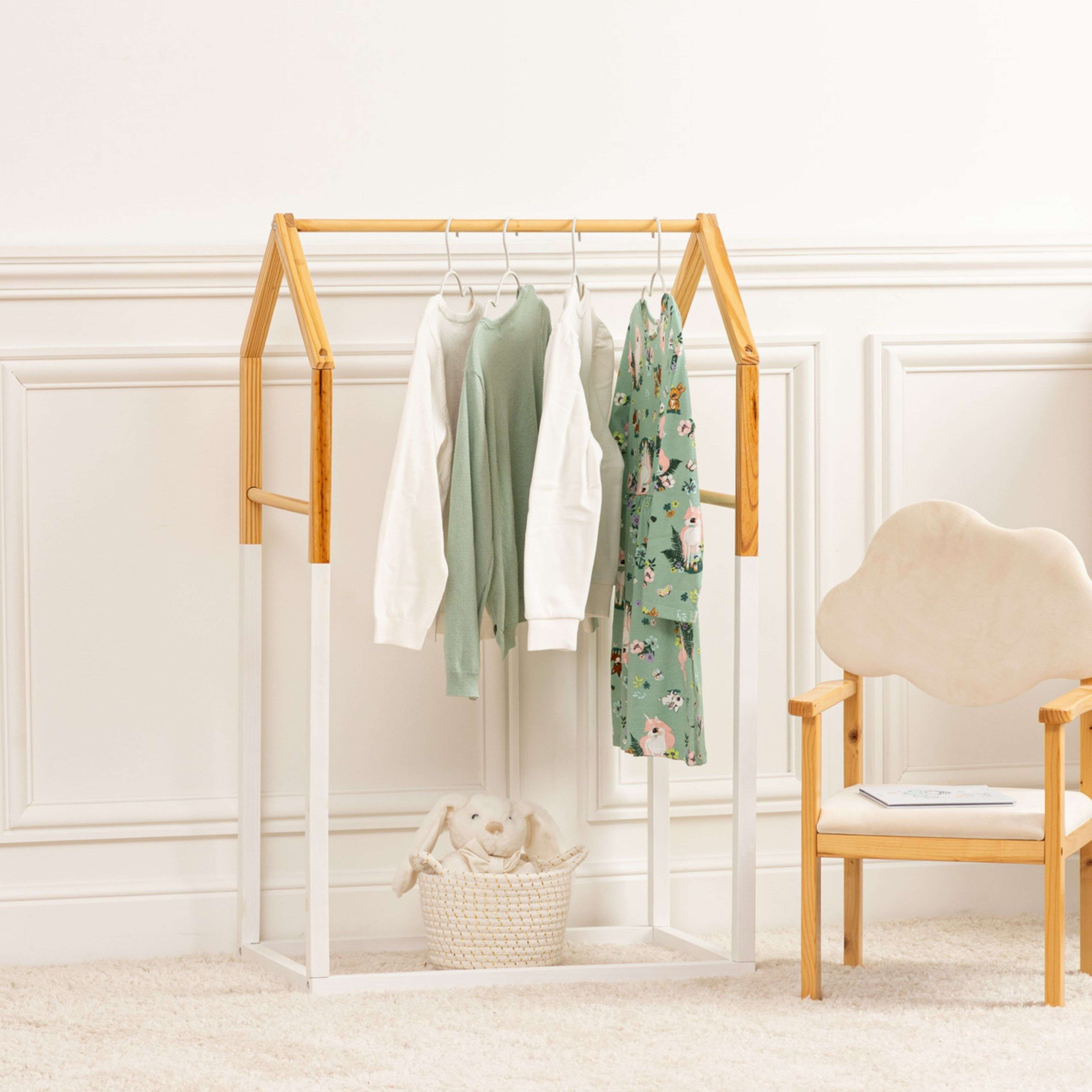 Un perchero de madera con ropa, una silla y una cesta con un conejo de peluche.