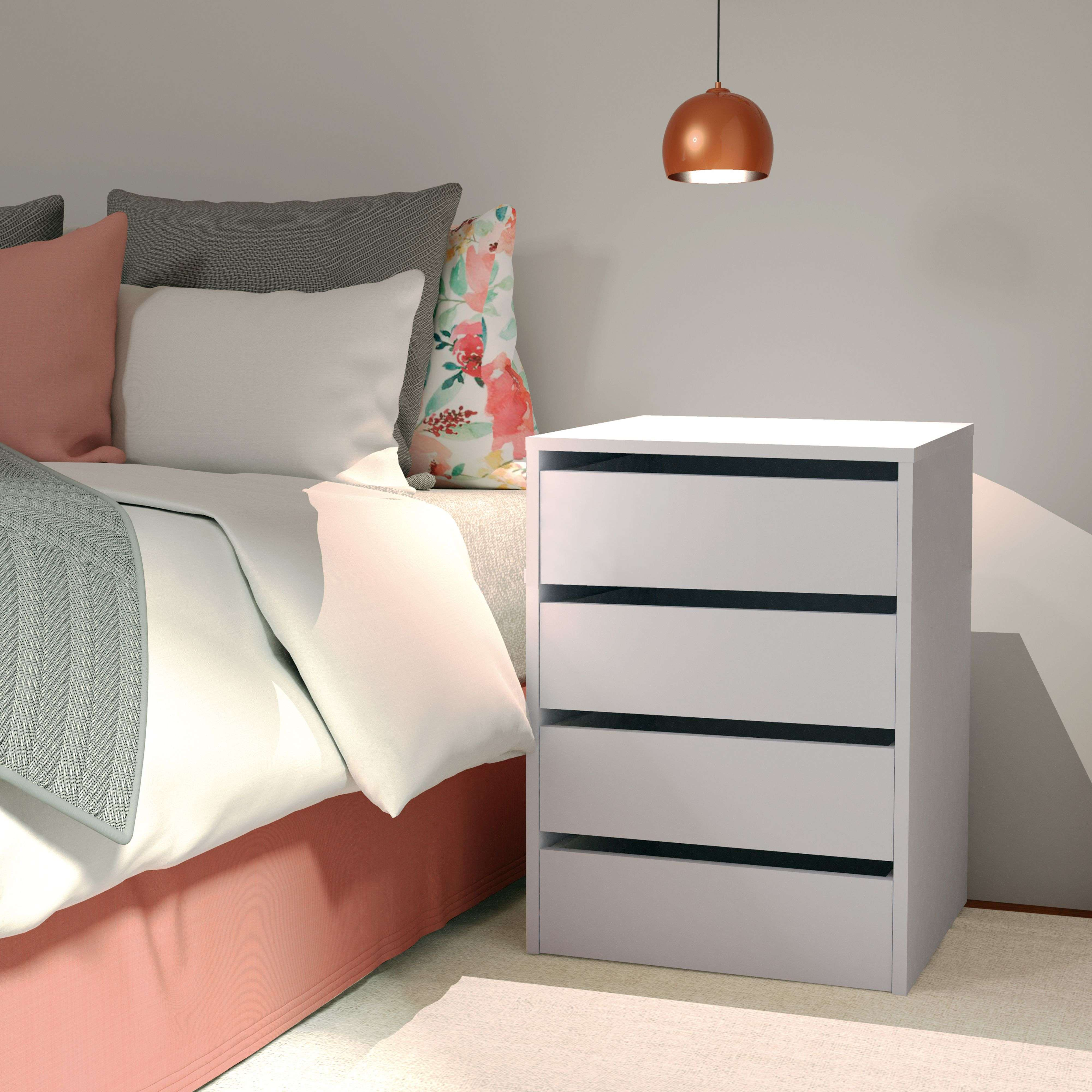 Una cama con almohadas rosas y florales junto a una mesita de noche blanca.