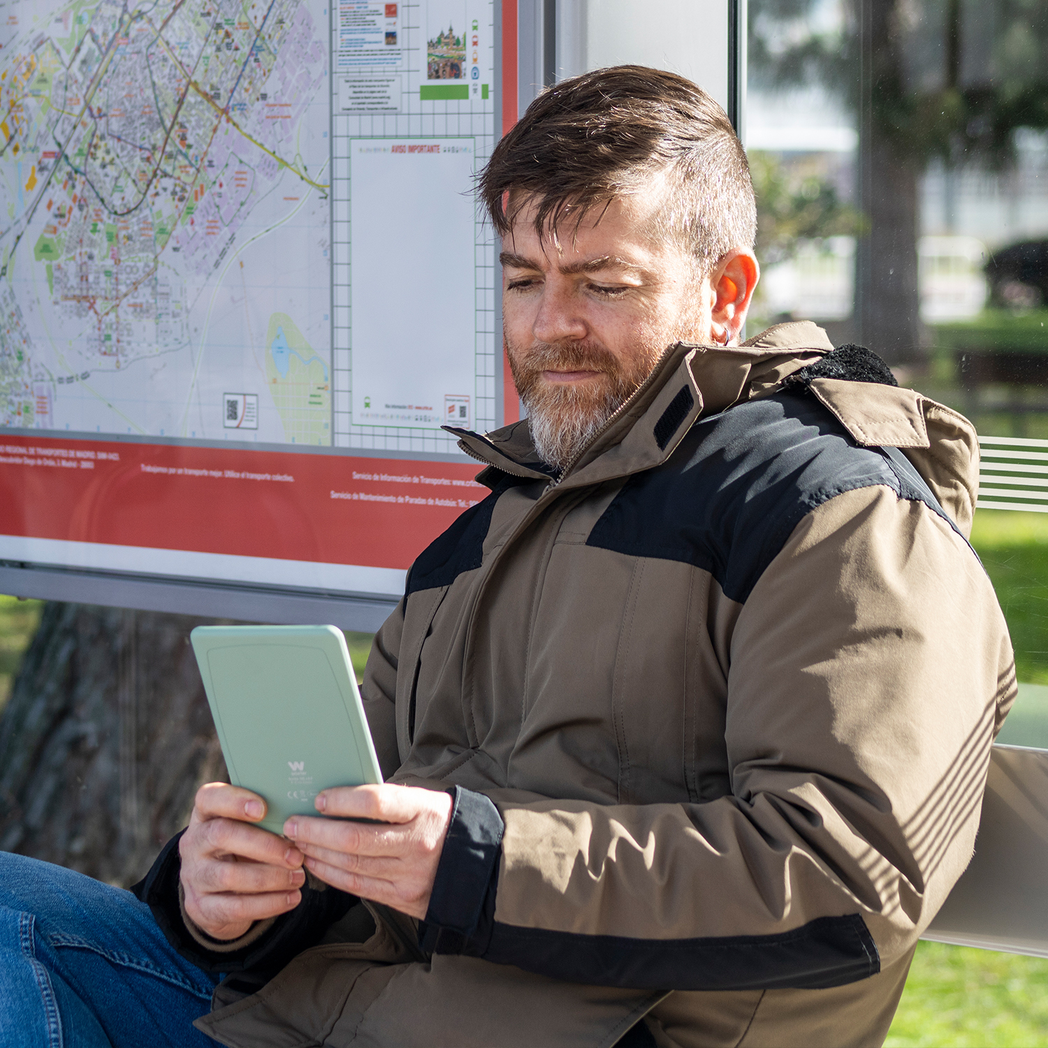 Un hombre se sienta en una parada de autobús, leyendo un e-reader.