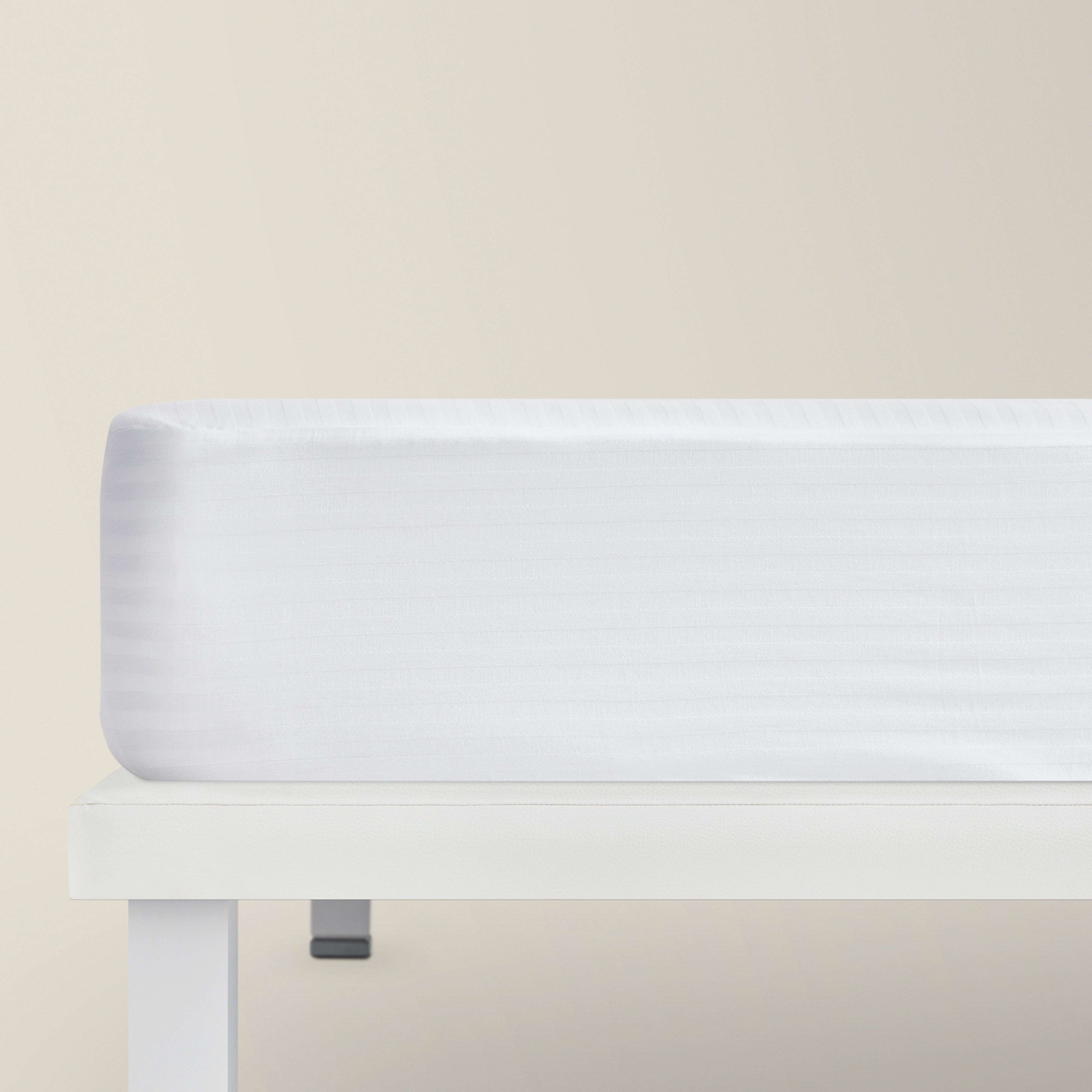 Una sábana bajera blanca con sutiles rayas sobre un somier blanco.