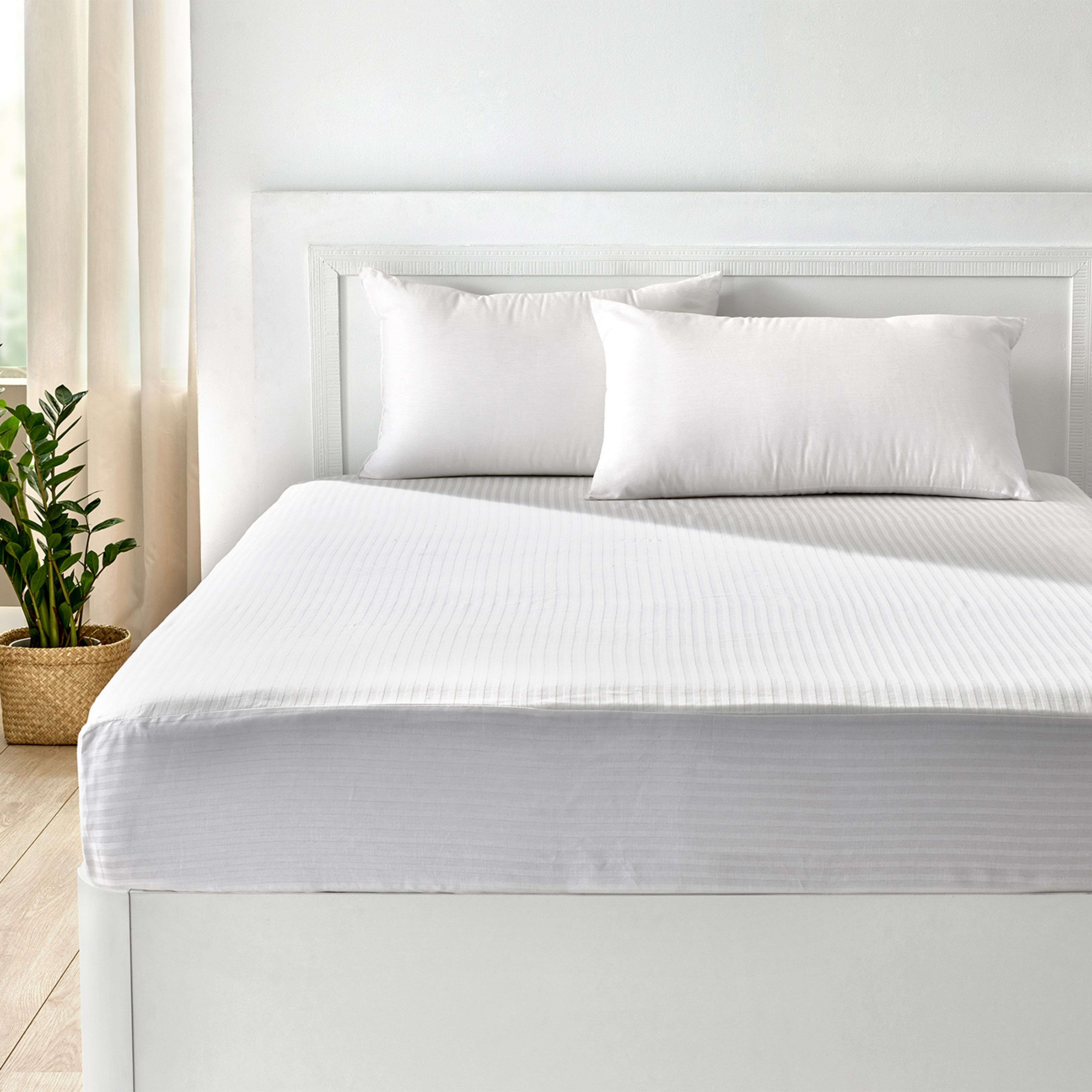 Una cama blanca con ropa de cama a rayas y dos almohadas blancas.