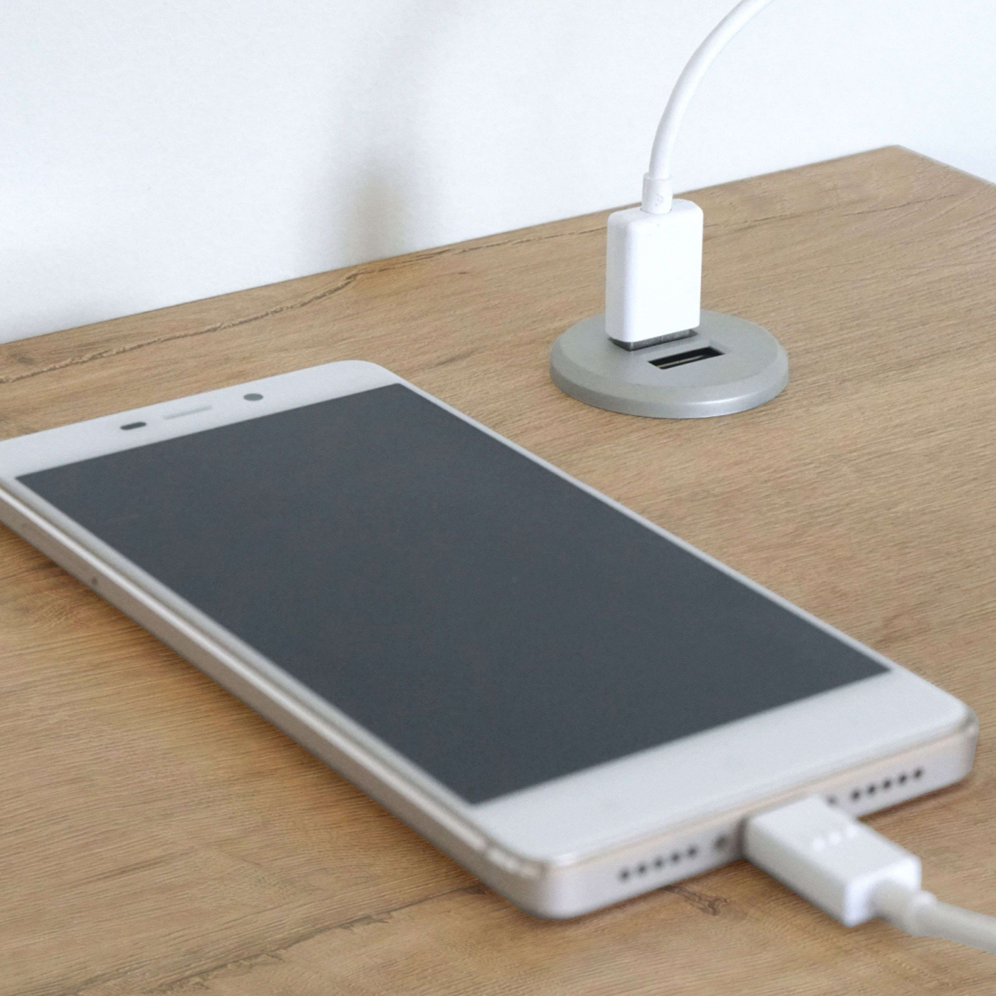 Un smartphone se carga en una mesa de madera con un cable blanco.