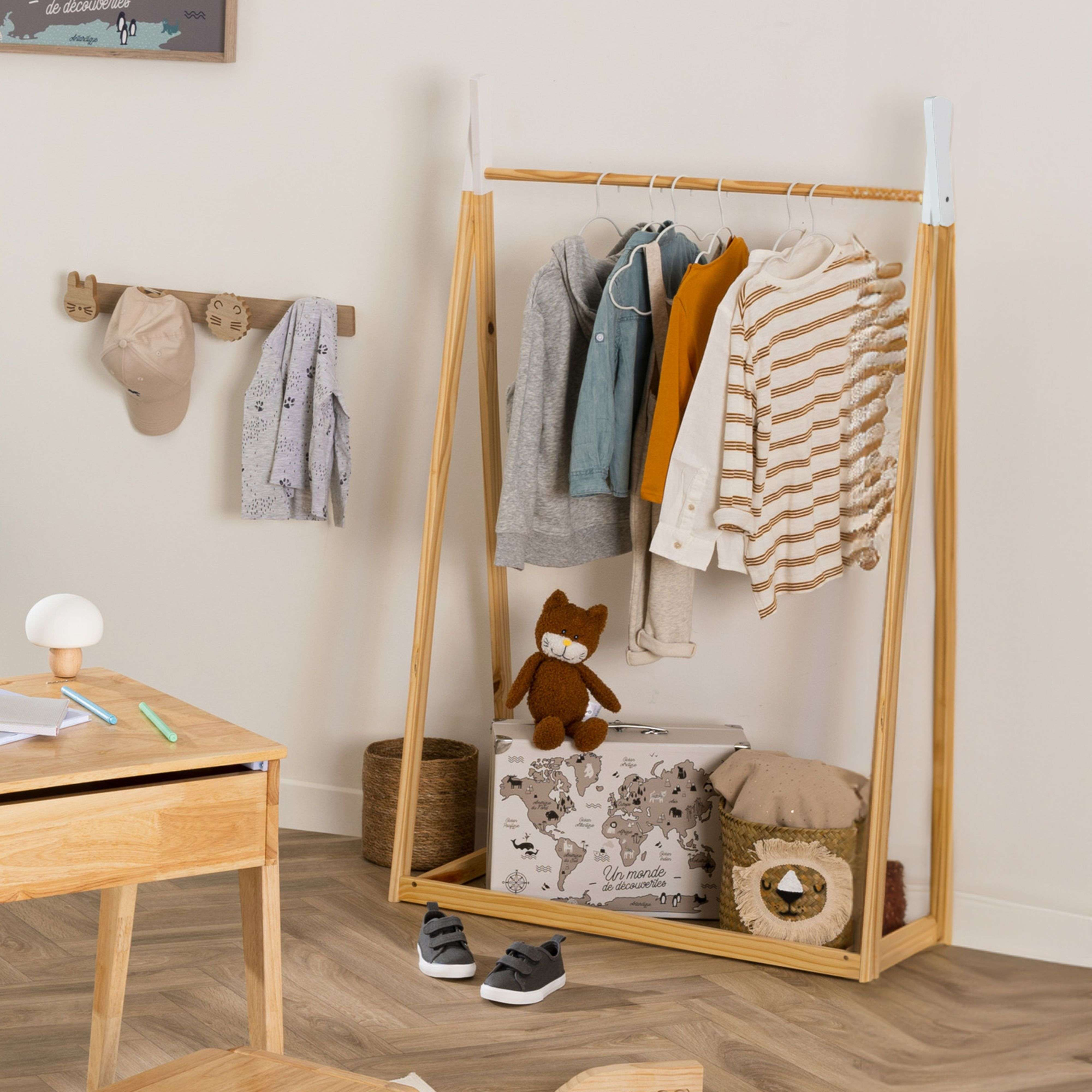 Un perchero de madera con ropa, un escritorio, un oso de peluche y una maleta.