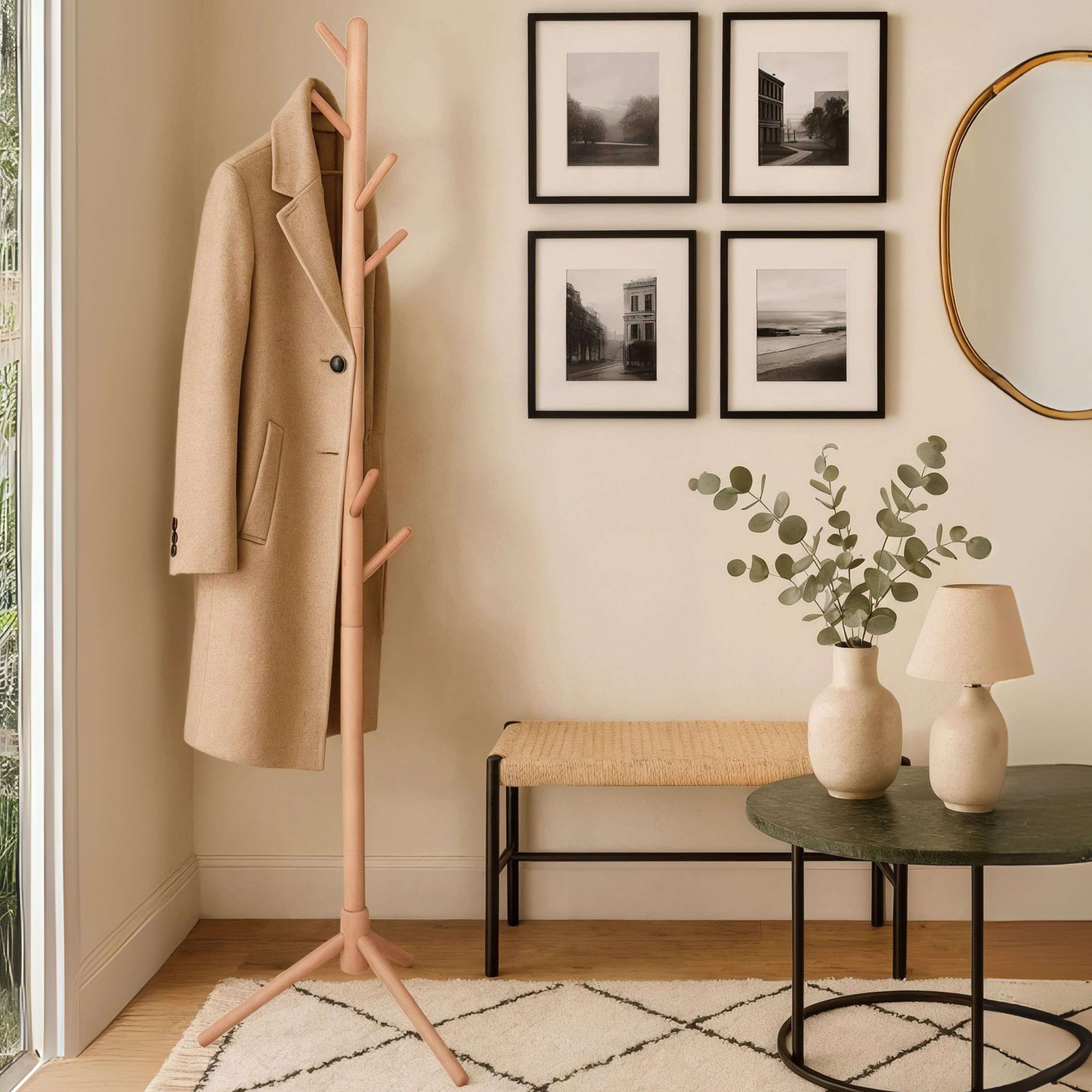 Un abrigo beige cuelga de un perchero de madera junto a una ventana.