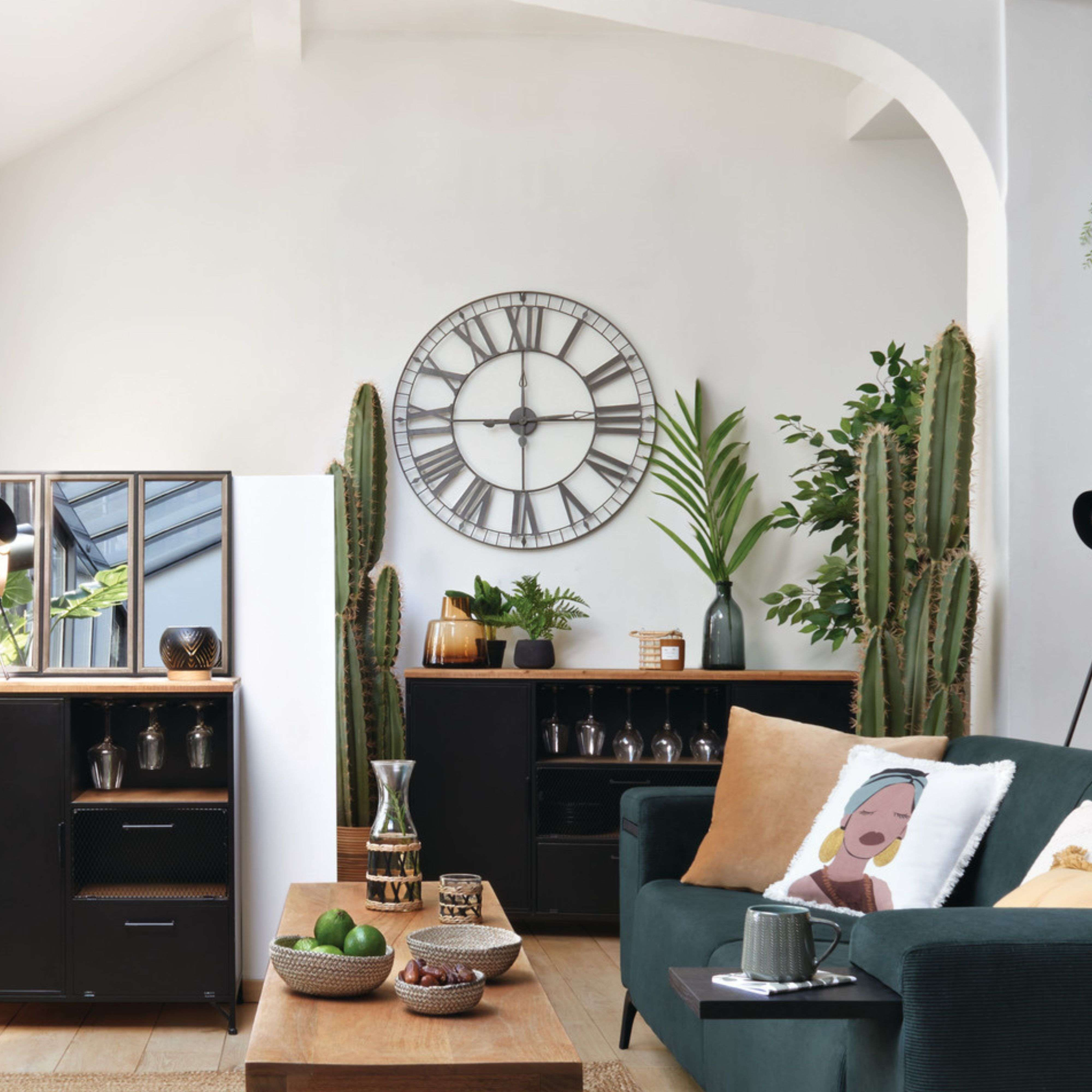Una sala de estar con sofá oscuro, plantas de cactus, un gran reloj de pared y mesa de madera.