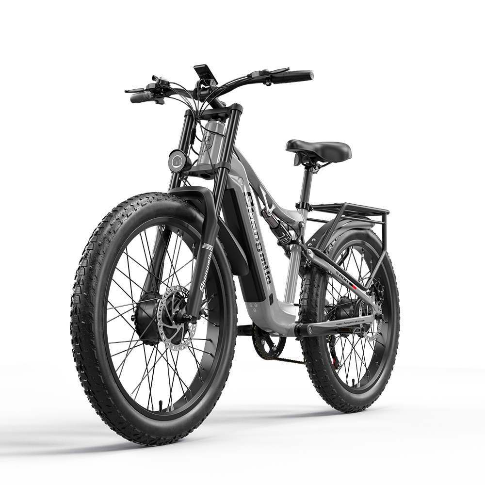 Ein graues Fatbike mit Federung und Gepäckträger steht vor weißem Hintergrund.