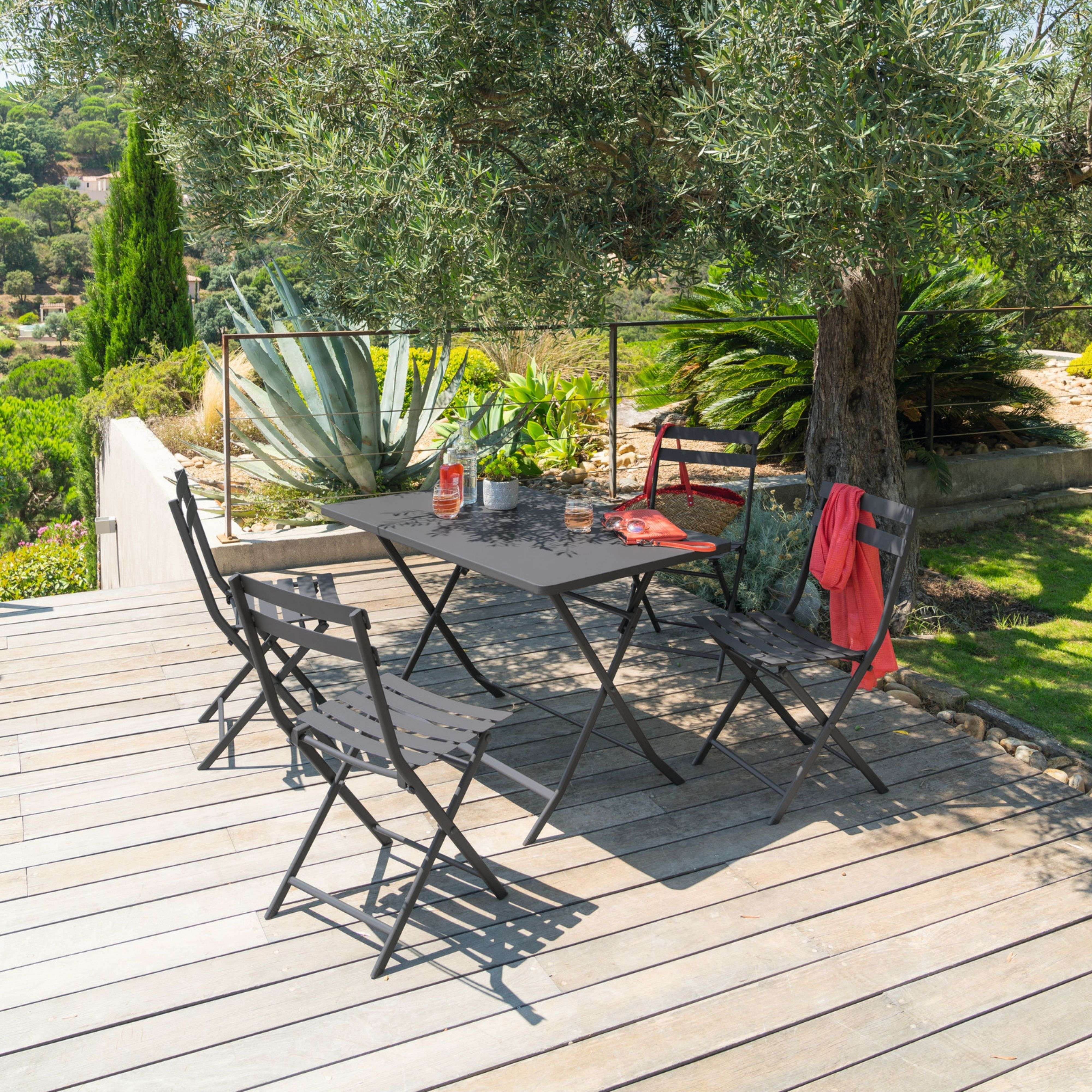 Una mesa de jardín y cuatro sillas en una terraza de madera bajo un olivo.