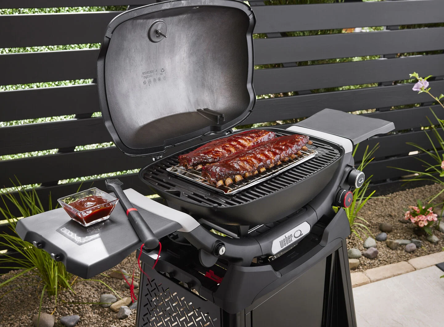 Zwei Rippchenstücke mit Glasur auf einem Grill mit Soßenschälchen und Pinsel daneben.