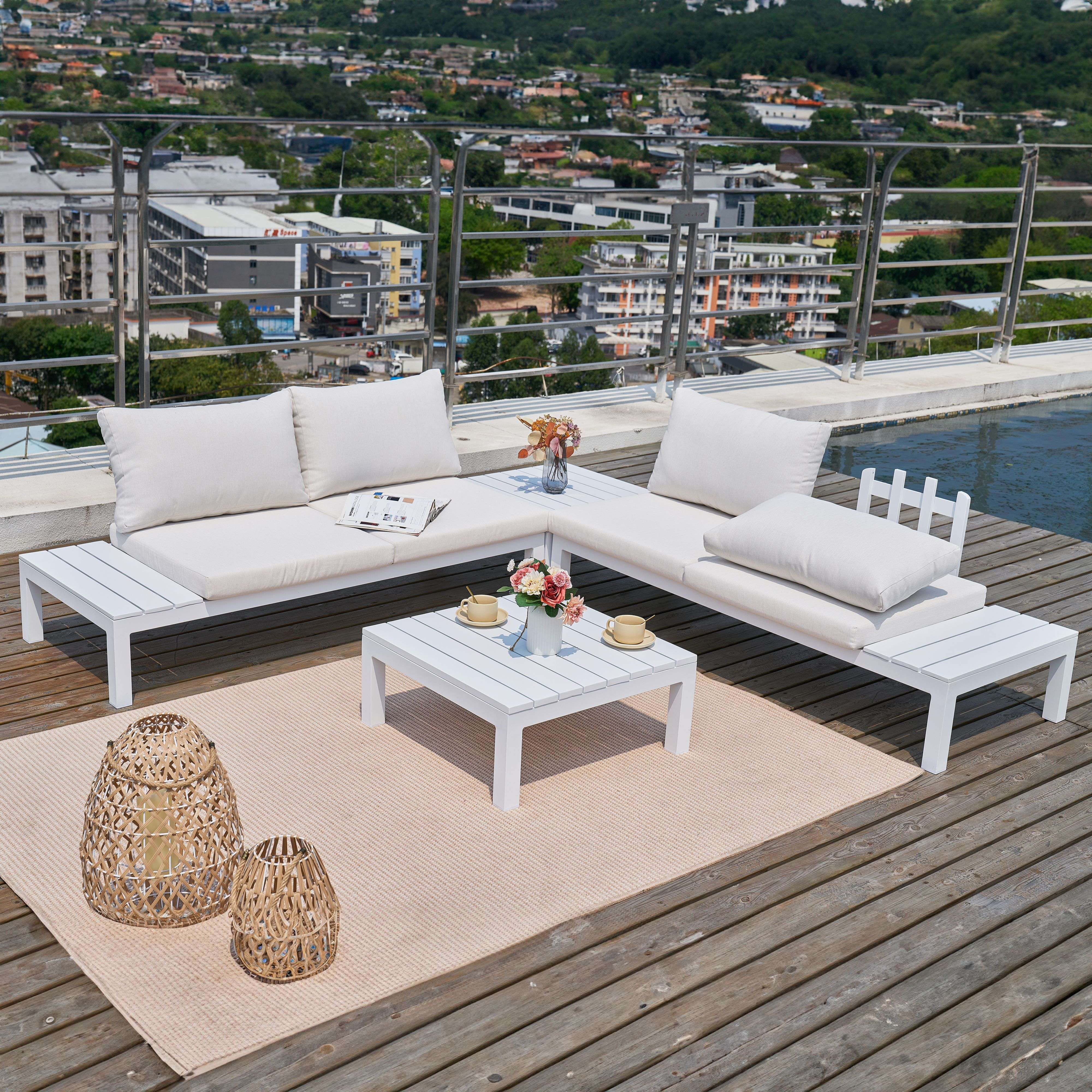 Muebles de salón blancos con cojines, mesa de centro, flores y cestas en tarima madera.