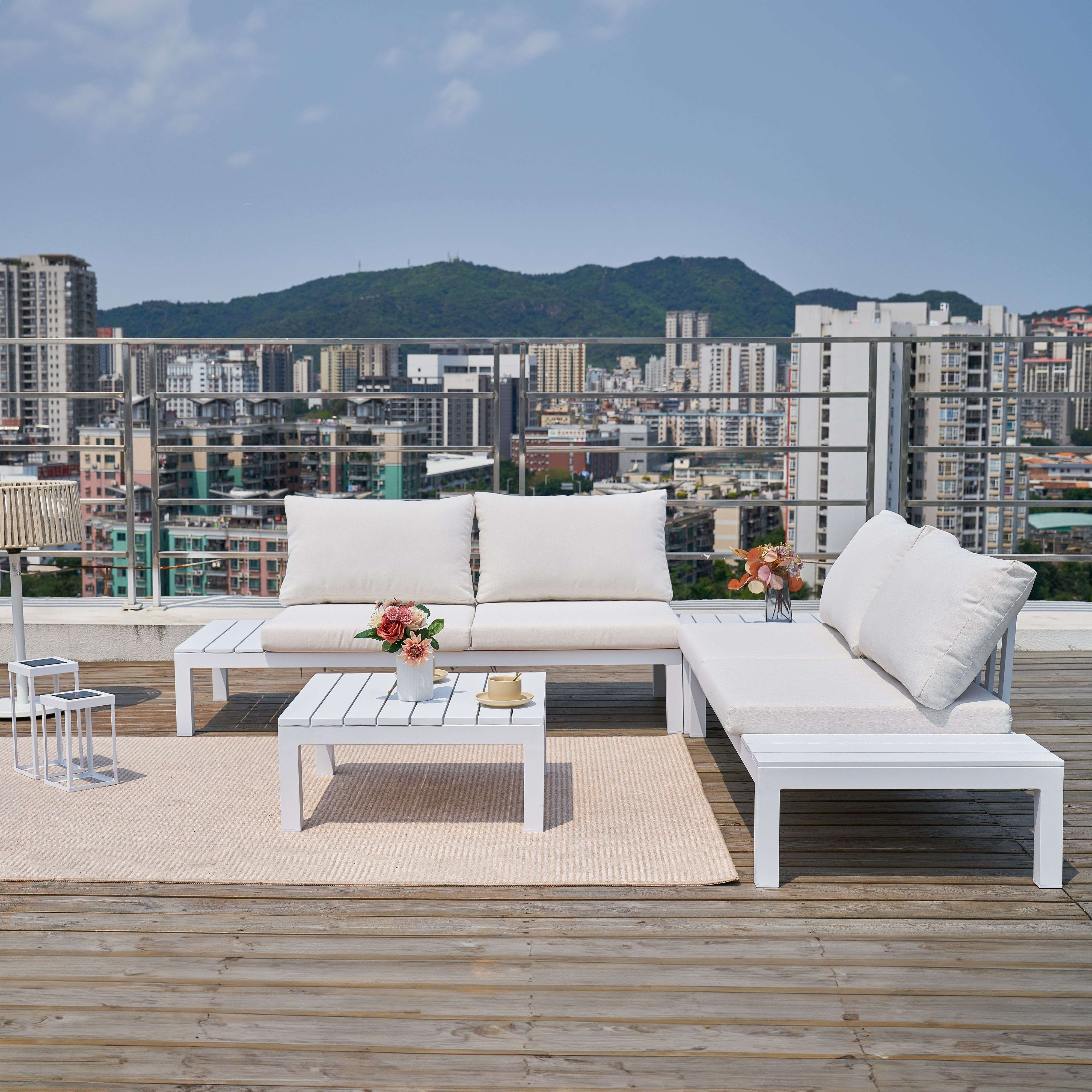 Muebles blancos de exterior en una terraza de madera, con vistas a la ciudad y montañas.