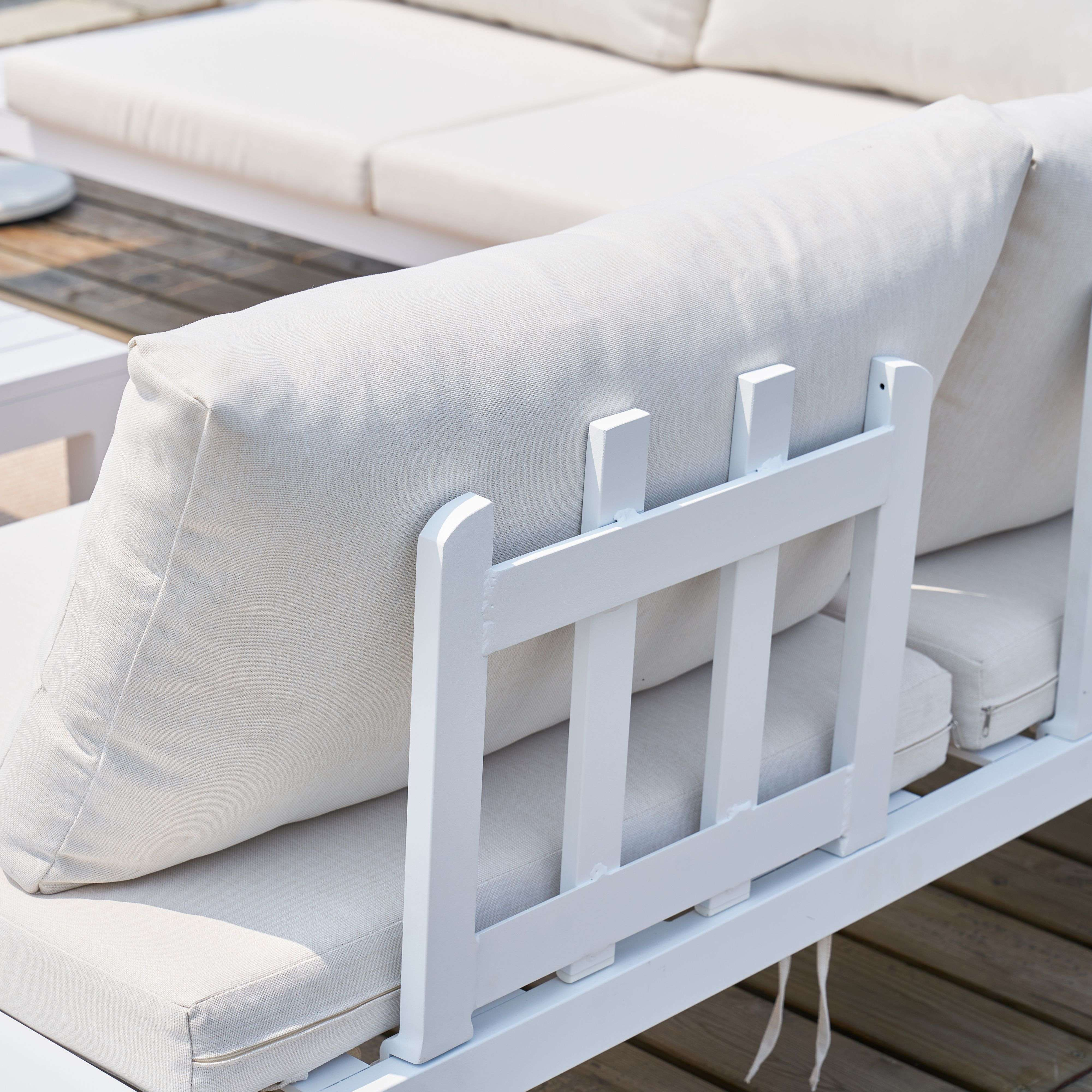 Sofá blanco de exterior con cojines color crema sobre tarima de madera.