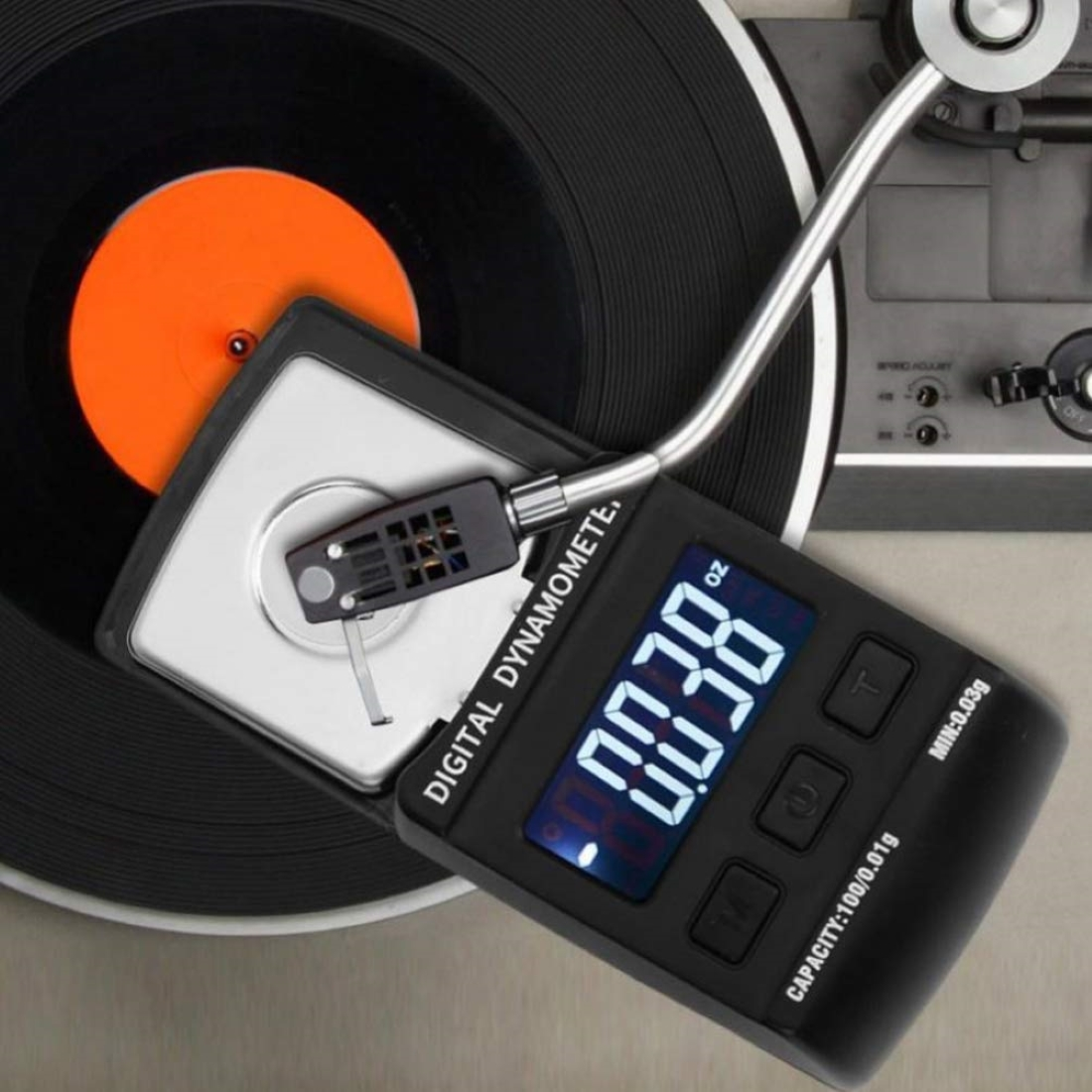 Una bilancia digitale poggia sul braccio di un giradischi, sopra un disco in vinile.